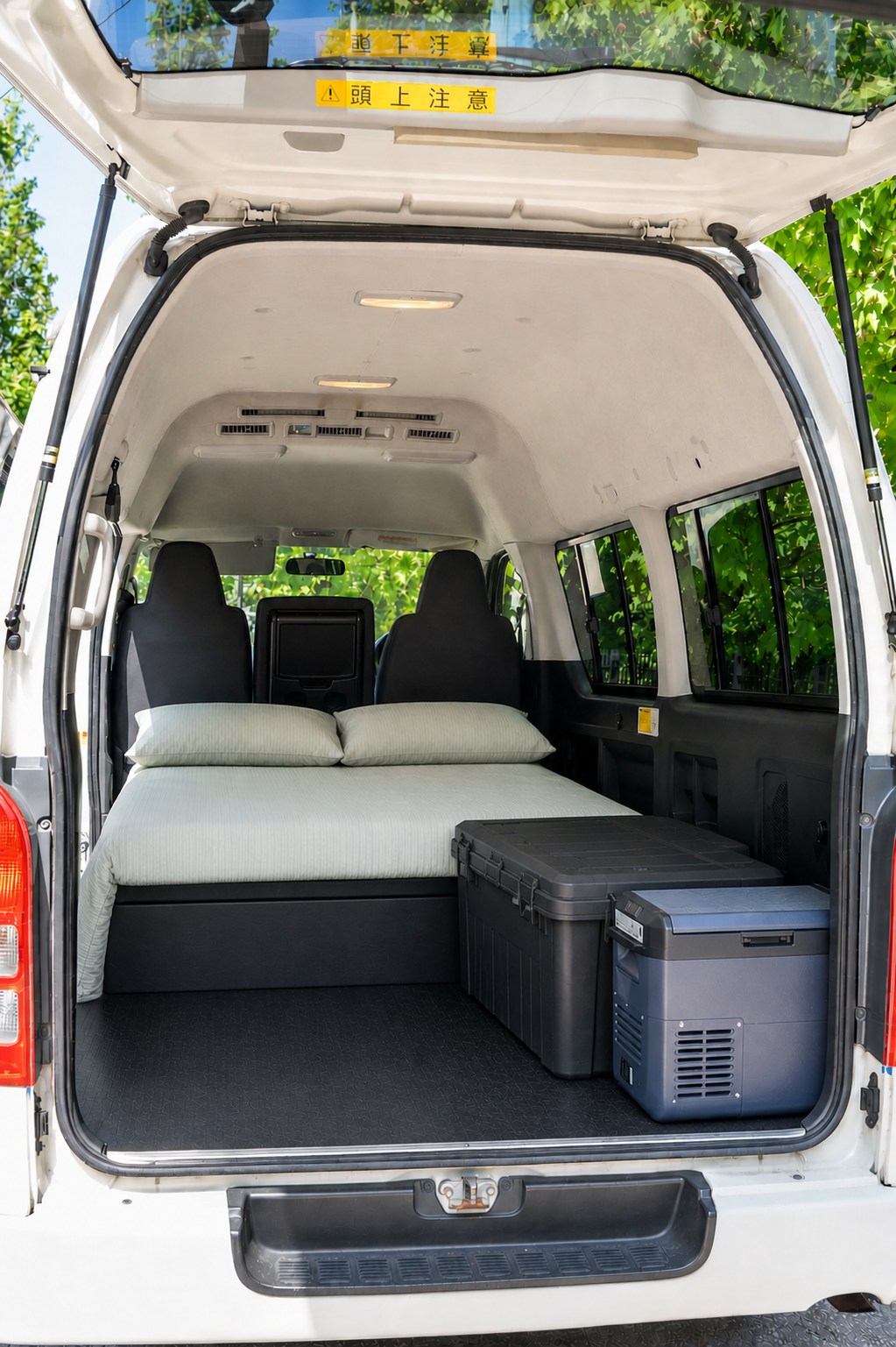 Inside this RV rental van's rear, a cozy bed, storage box, and portable fridge offer comfort for travelers.. Toyota Hiace 2005