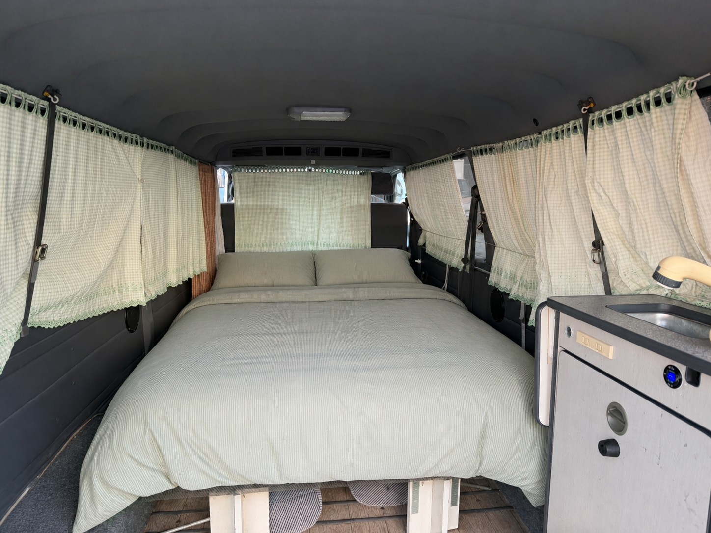 Cozy rv rental campervan interior features a comfy bed with striped bedding, charming gingham curtains, and a compact kitchenette.. Toyota Hiace 2003