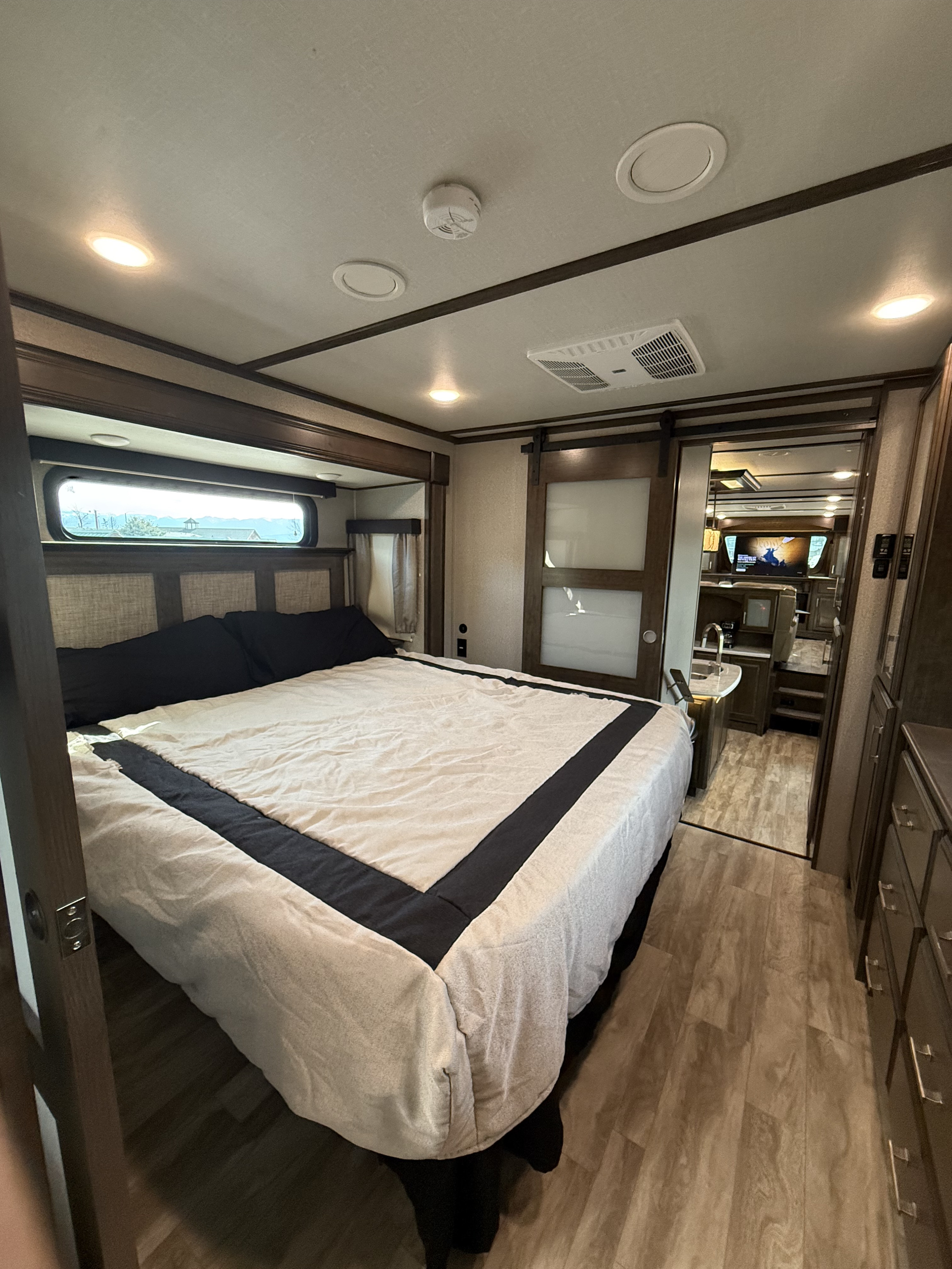 Inside a modern rv rental, a cozy bedroom with a large bed, window with a view, and sliding barn doors opening to the living space.. Grand Design Solitude 2020