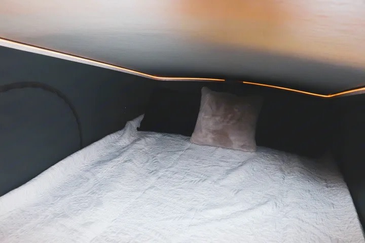 Relaxing RV rental bed with white quilt, pink pillow, and ambient LED strip lighting in a compact interior.. Winnebago Solis 2023
