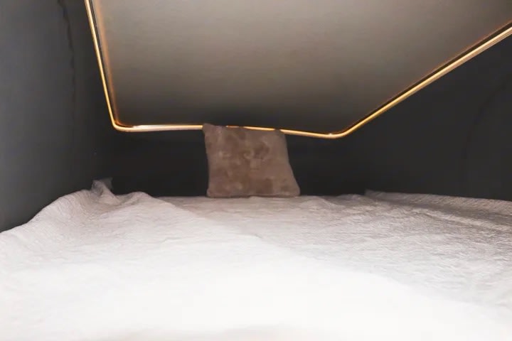 Cozy RV rental sleeping area featuring a bed with white bedding and warm ambient lighting. Perfect for your camper van adventures.. Winnebago Solis 2023