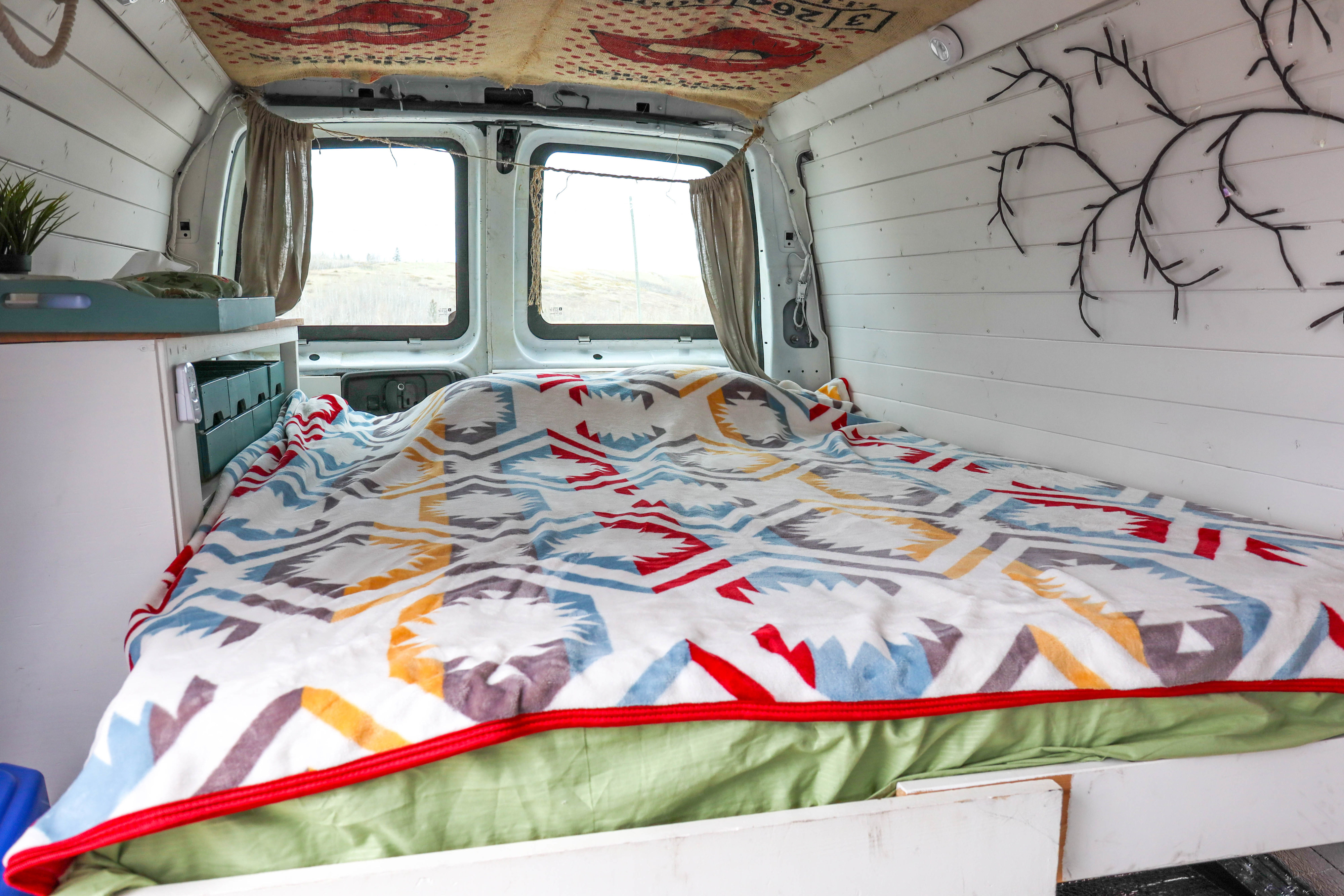 Cozy RV rental interior featuring a colorful patterned bed, panoramic windows, wooden paneling, and string lights.. Gmc savana 2500 2008