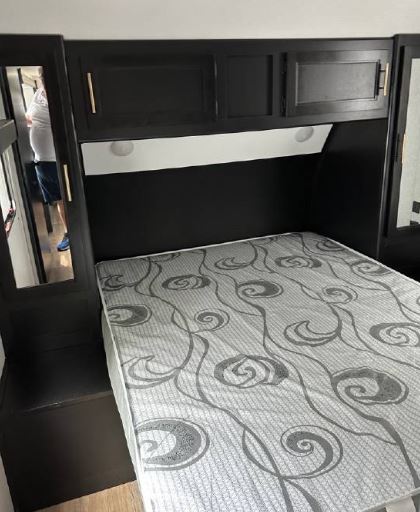 RV rental bedroom featuring a bed with a gray swirl mattress, dark wood overhead cabinets, and built-in side storage.. Forest River Cherokee Grey Wolf 2022