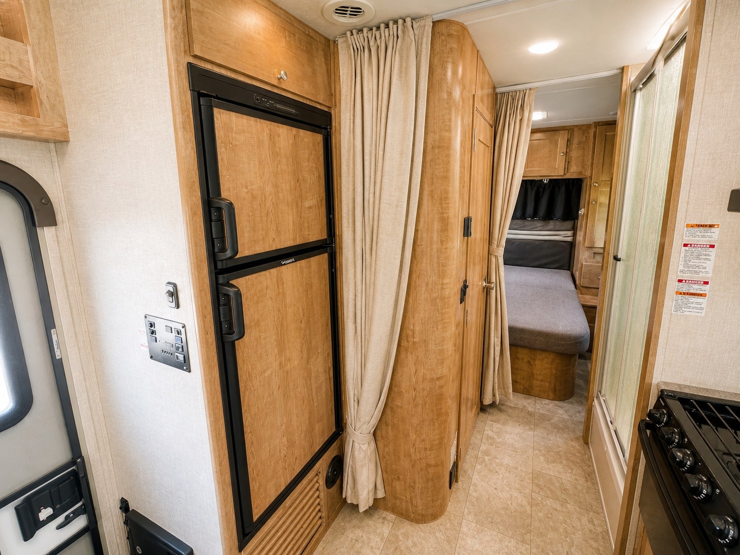 RV rental interior: A compact motorhome showing the kitchen area with a fridge, control panel, and a curtained sleeping nook.. Forest River Coachmen Leprechaun 2020