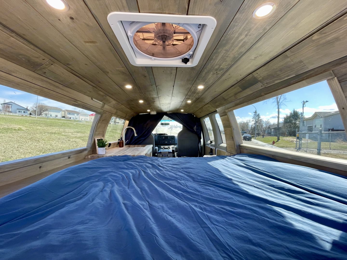 This cozy RV rental shows a wood-paneled interior, a comfy blue bed, kitchenette, and scenic views, perfect for van life.. Ford E350 extended 2011
