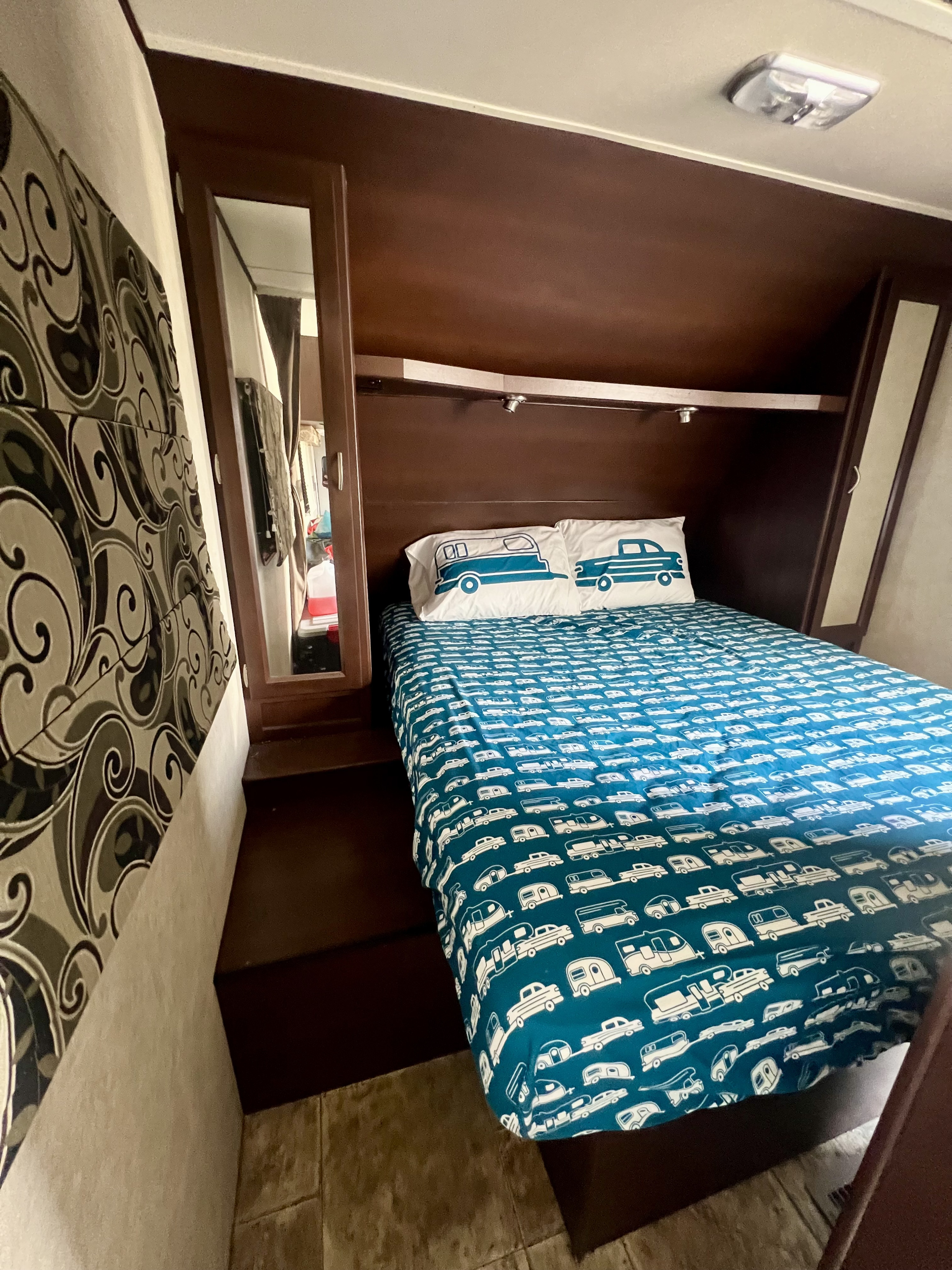 RV rental bedroom features a comfy bed with camper-themed bedding, dark wood cabinets, and mirrored closet doors.. Crossroads Sling Shot 2012