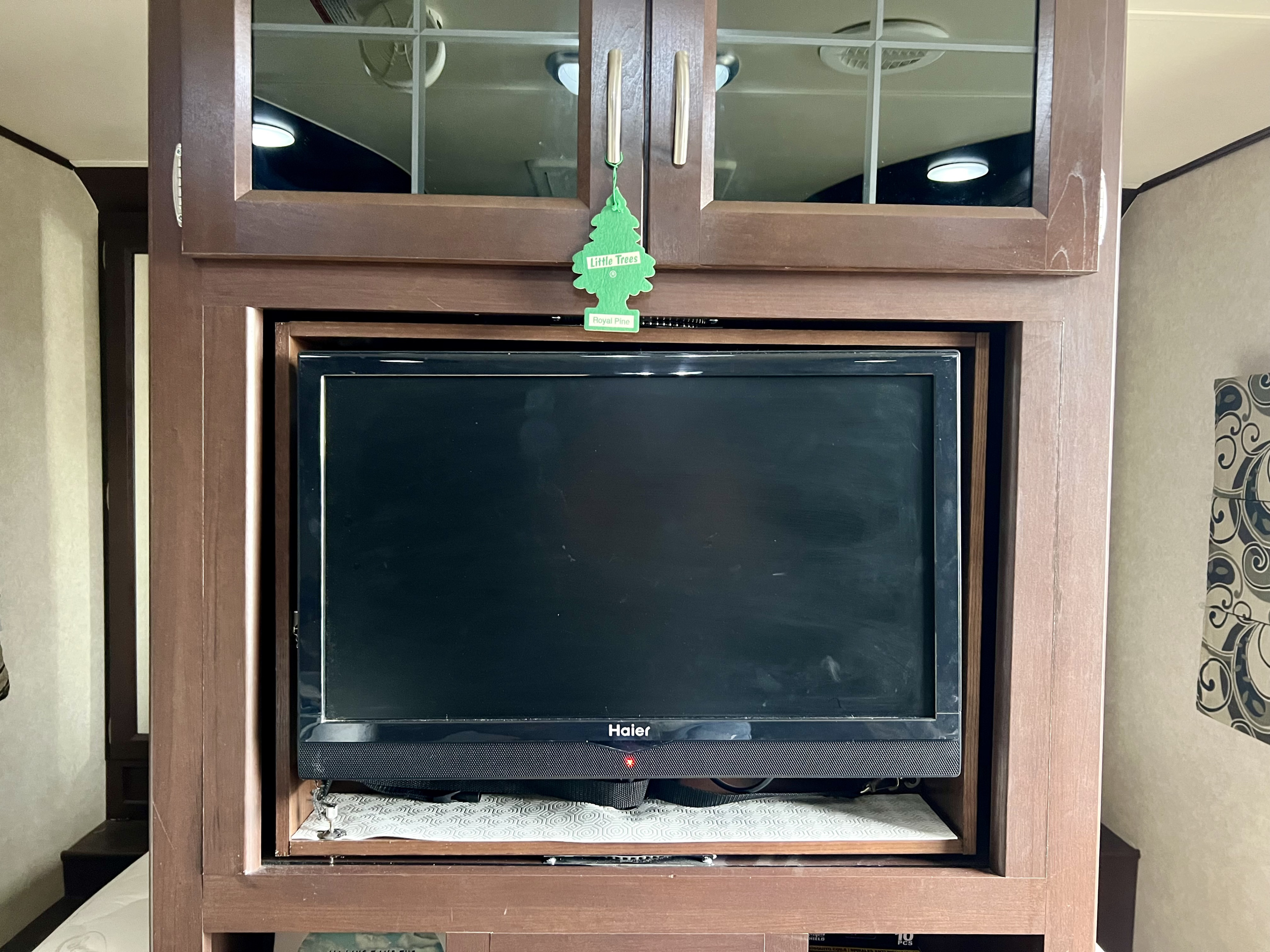 Recessed Haier TV in a wooden cabinet, with a "Little Trees" air freshener above, typical for an RV rental interior.. Crossroads Sling Shot 2012