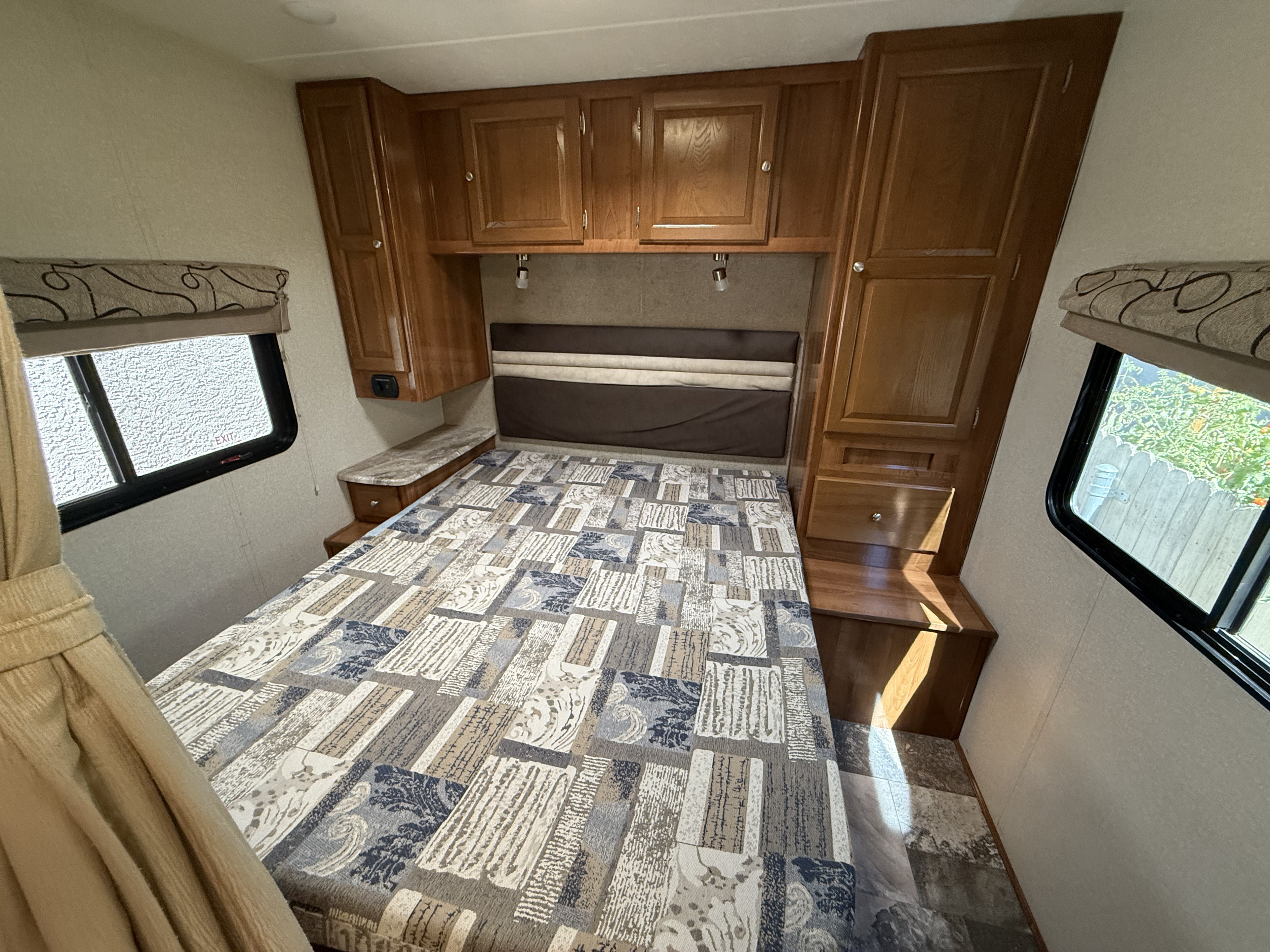 Inside a comfy **rv rental** bedroom: features a patterned bed, wood storage, and natural light from side windows.. Coachmen Leprechaun 2019