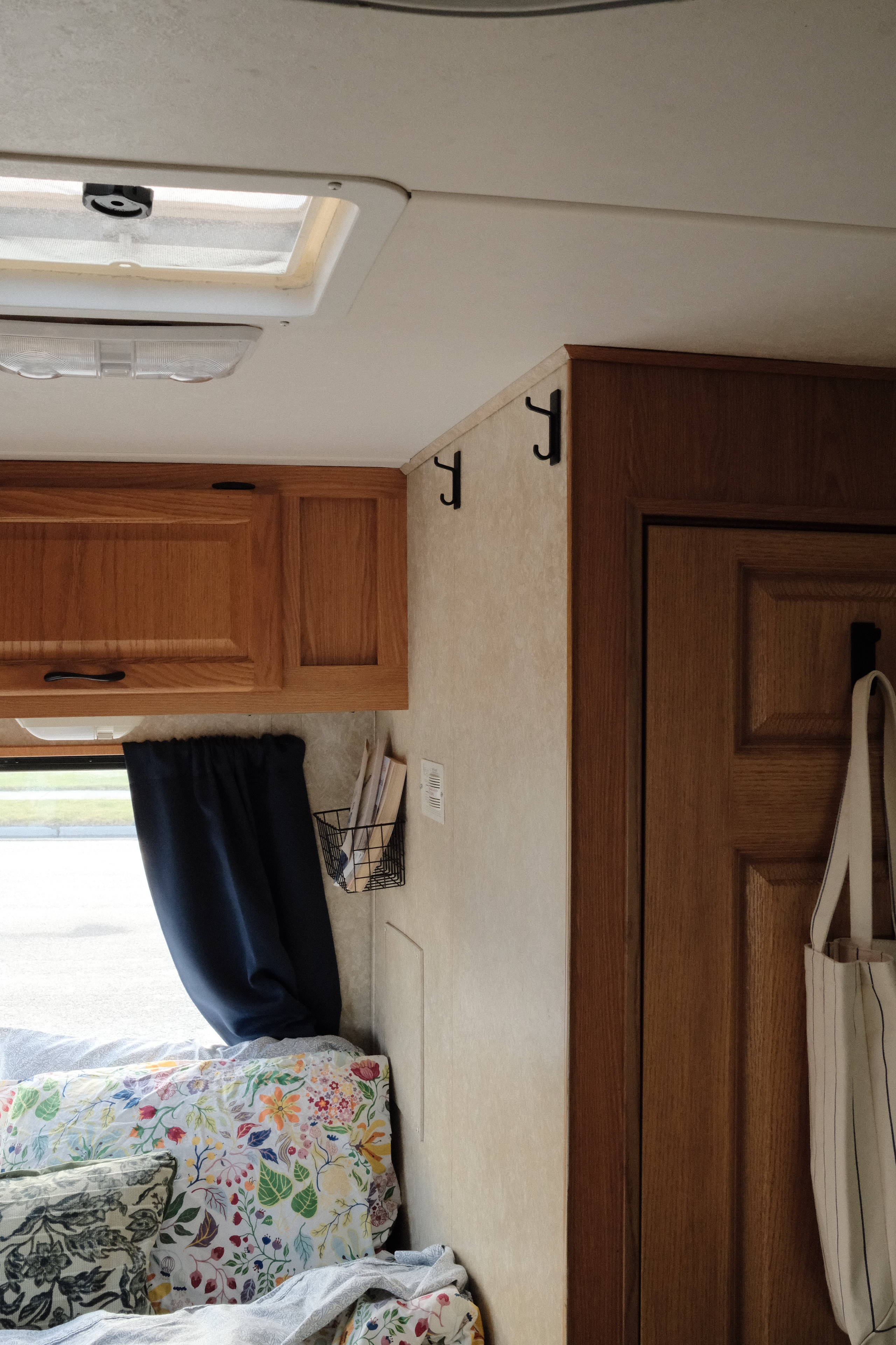 Inside an RV rental: overhead wood cabinets, window with curtain, wall hooks, storage basket, and floral pillows.. Four Winds Majestic 2006