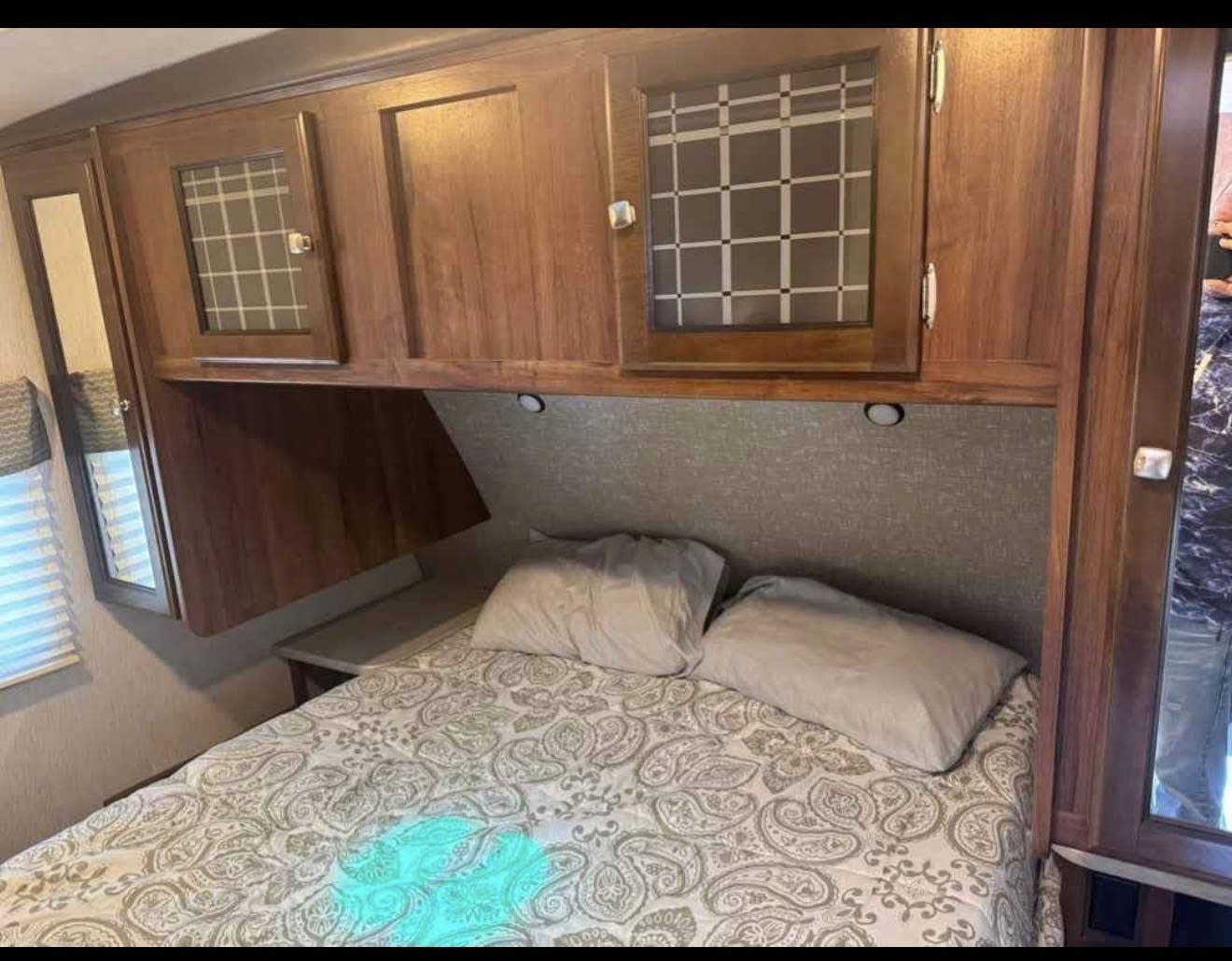 Cozy RV rental bedroom featuring a patterned bed, pillows, wood cabinets, and window blinds. Ready for your next adventure!. Heartland RVs Mallard 2018