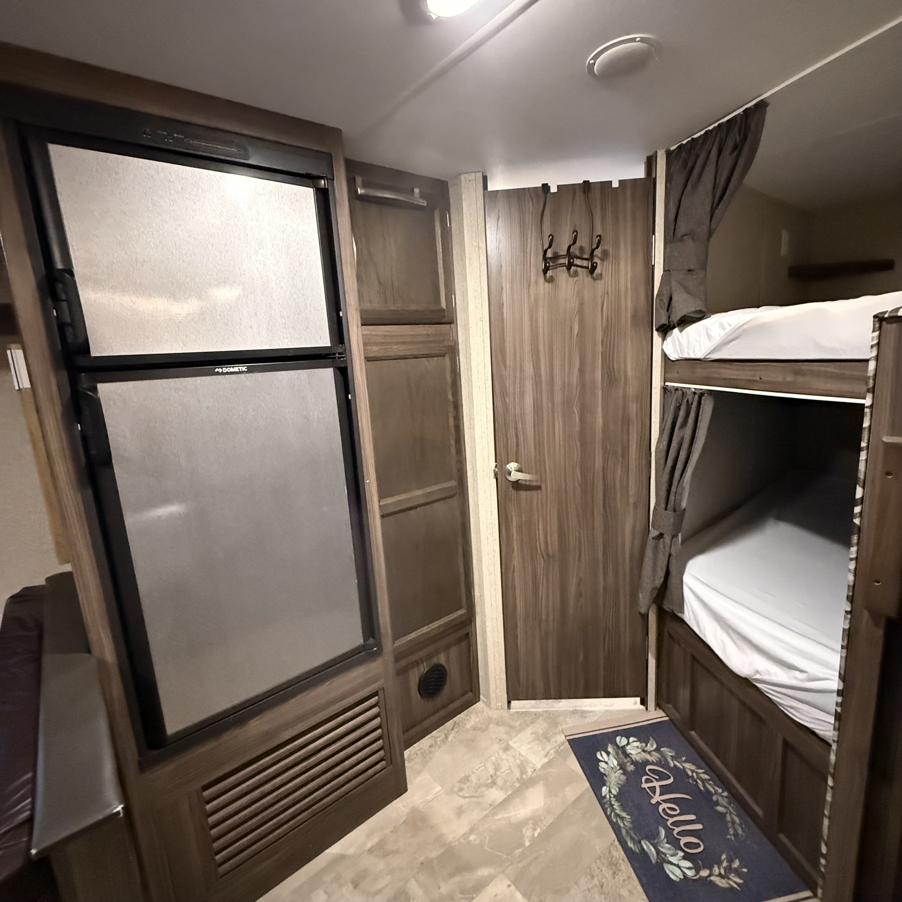 Cozy RV rental interior featuring a refrigerator, storage, and bunk beds with privacy curtains.. Coachmen Apex 2018