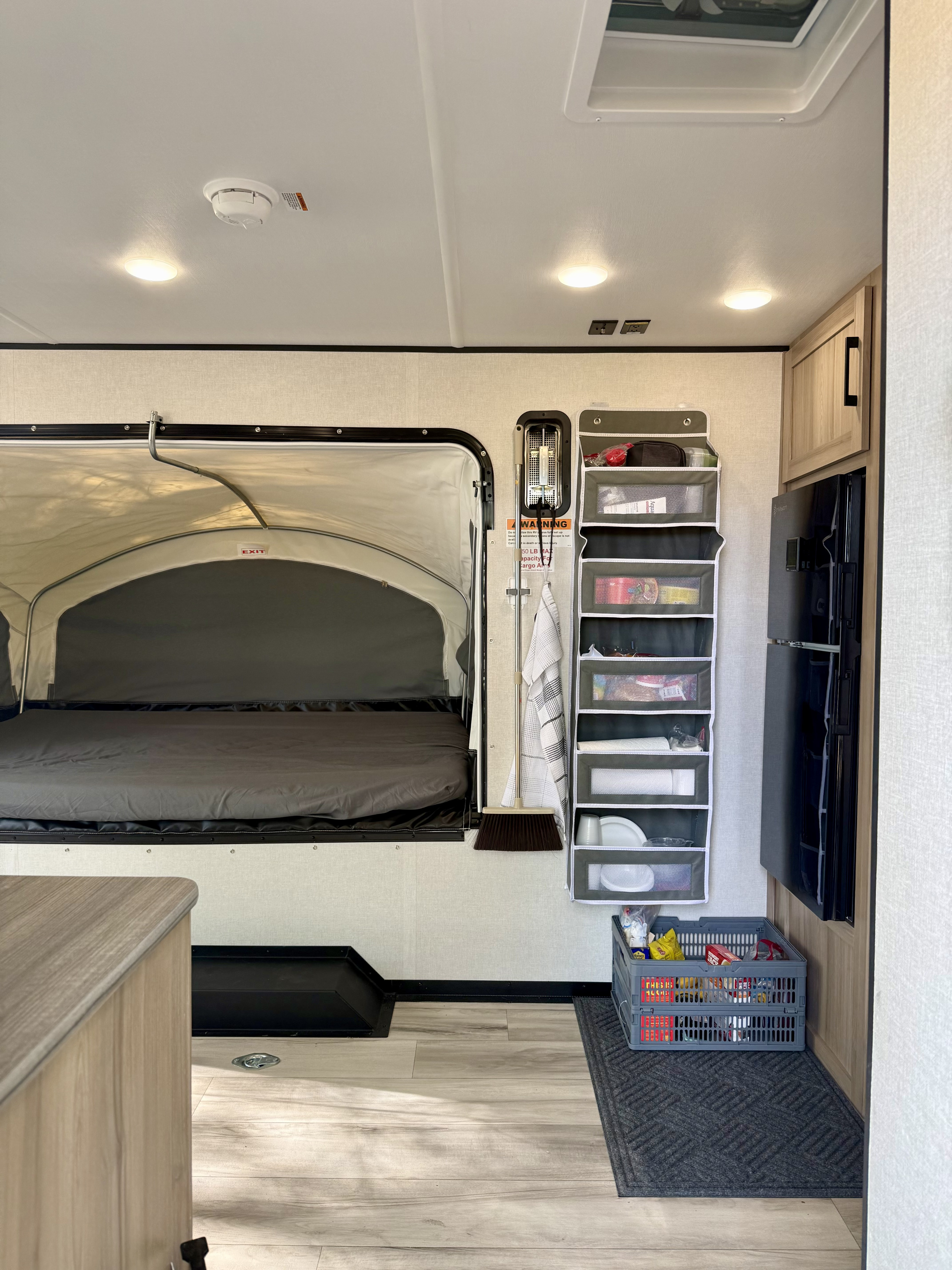 RV rental interior: A compact living space with a pop-out bed, vertical storage organizer, and refrigerator.. Keystone Coleman 13T 2026