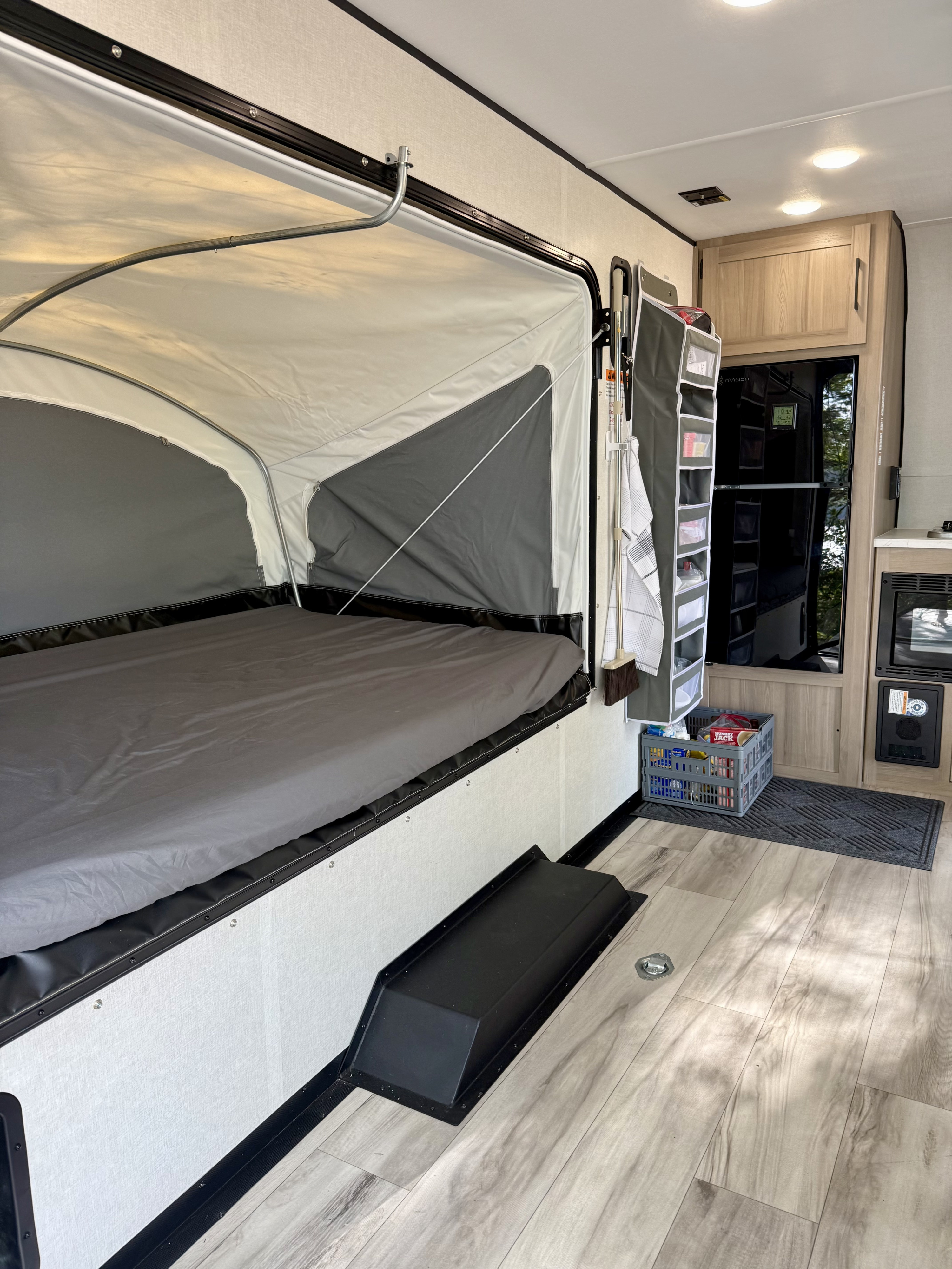 Pop-up RV rental interior: large fold-out bed, kitchenette with fridge, and clever hanging storage. Ready for adventure!. Keystone Coleman 13T 2026