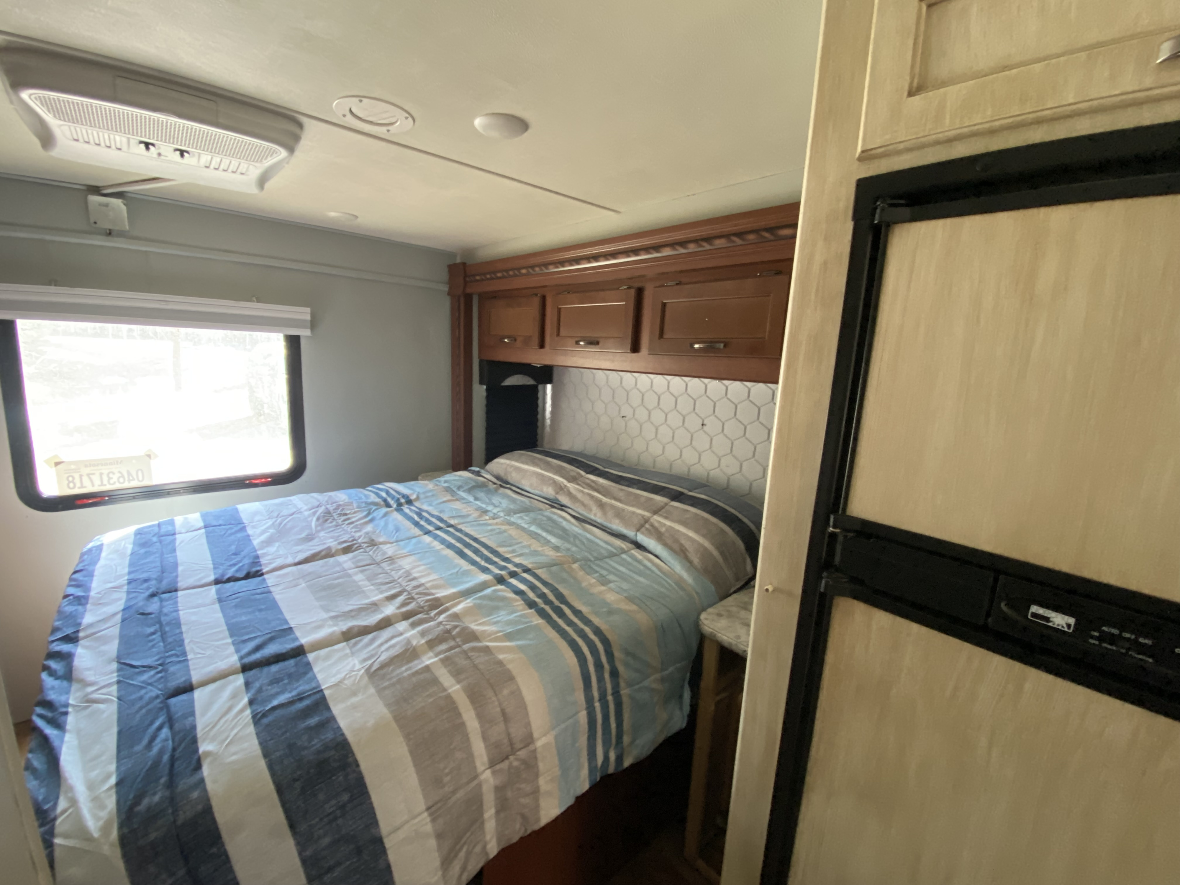 RV rental bedroom: striped bed, overhead storage, window, and small fridge. Compact & cozy for road trips.. Thor Freedom Elite 2016