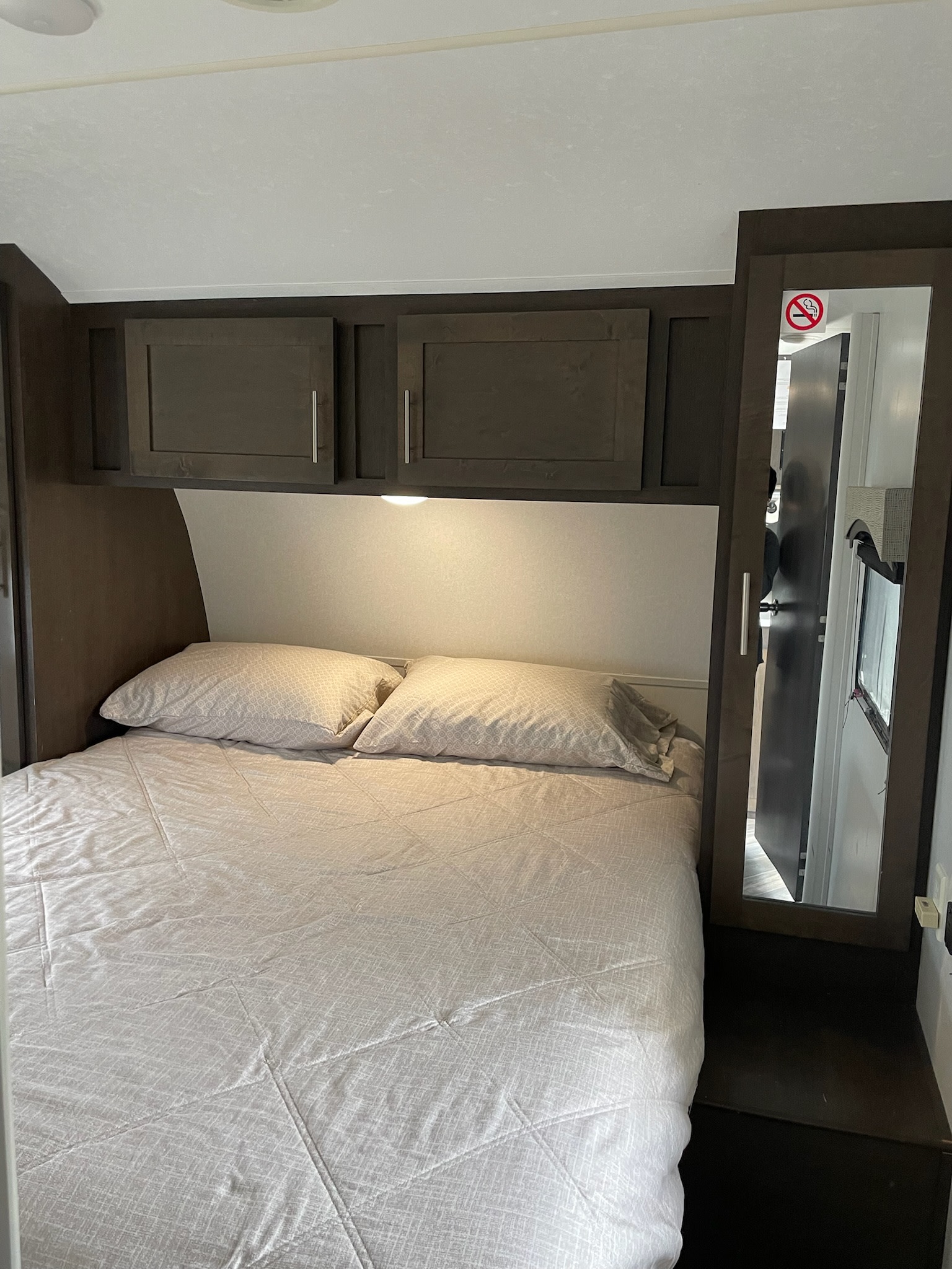 Cozy RV rental bedroom featuring a comfortable bed with overhead storage cabinets and a mirror. Perfect for your next adventure.. Forest River EVO 2019