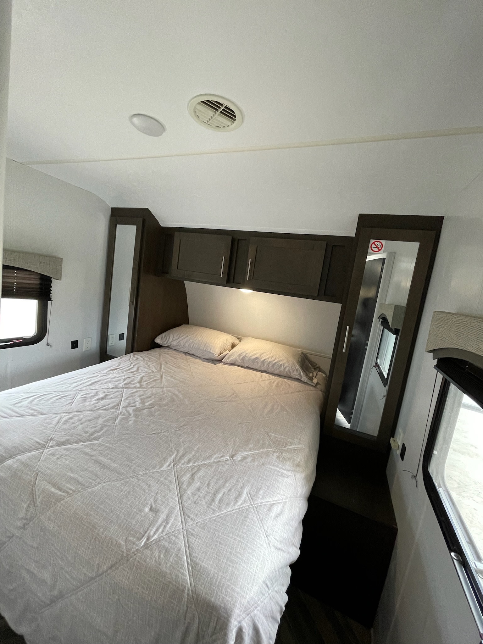 Cozy RV rental bedroom with dark wood cabinets, comfy bed, and a mirrored closet.. Forest River EVO 2019