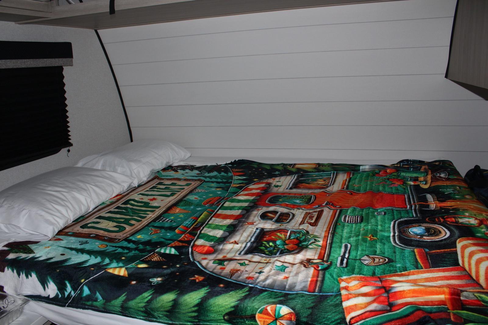 RV rental interior showing a cozy bed with white pillows and a colorful "CAMP LIFE" blanket, set against shiplap walls.. Ranger Colt 17Db 2026