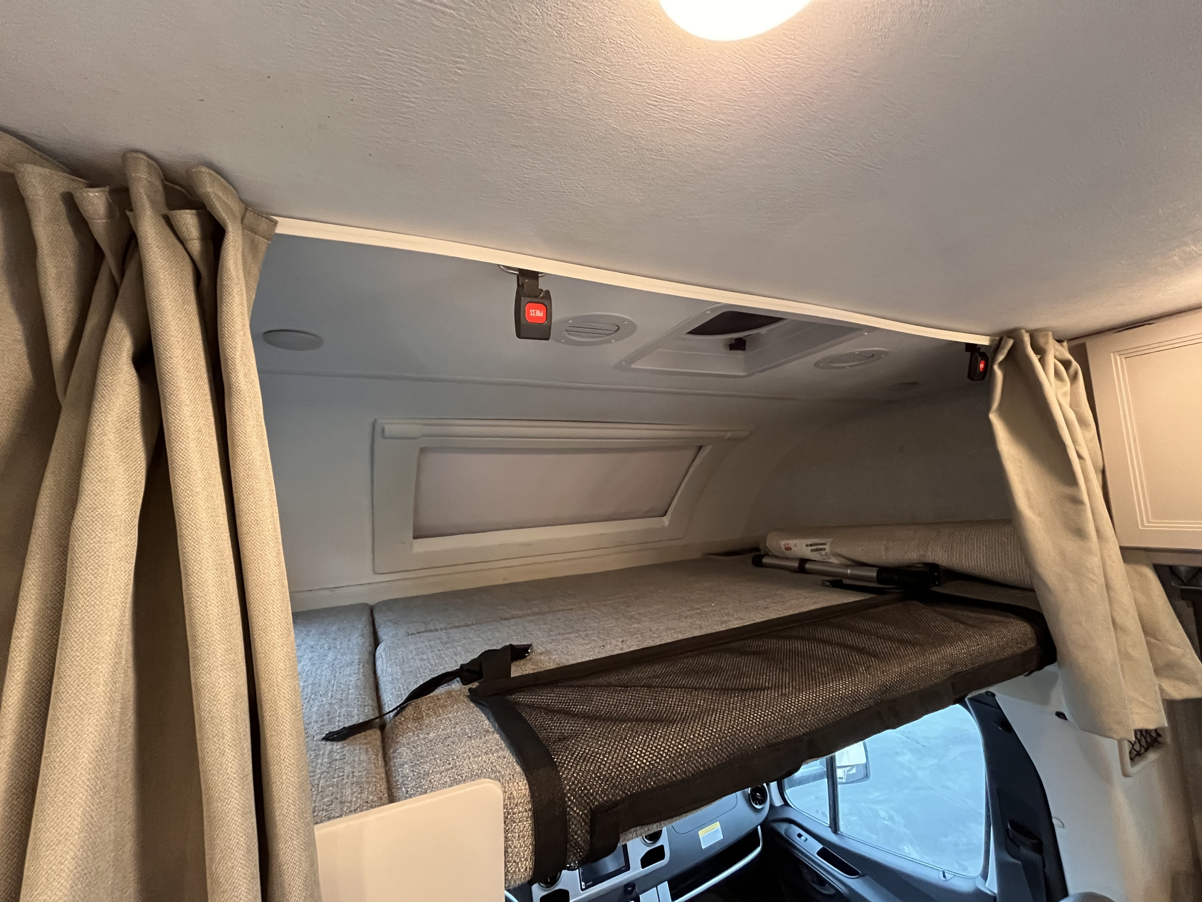 Overhead bunk bed inside an RV rental, featuring a safety net, window, and privacy curtains.. Thor Quantum 2022