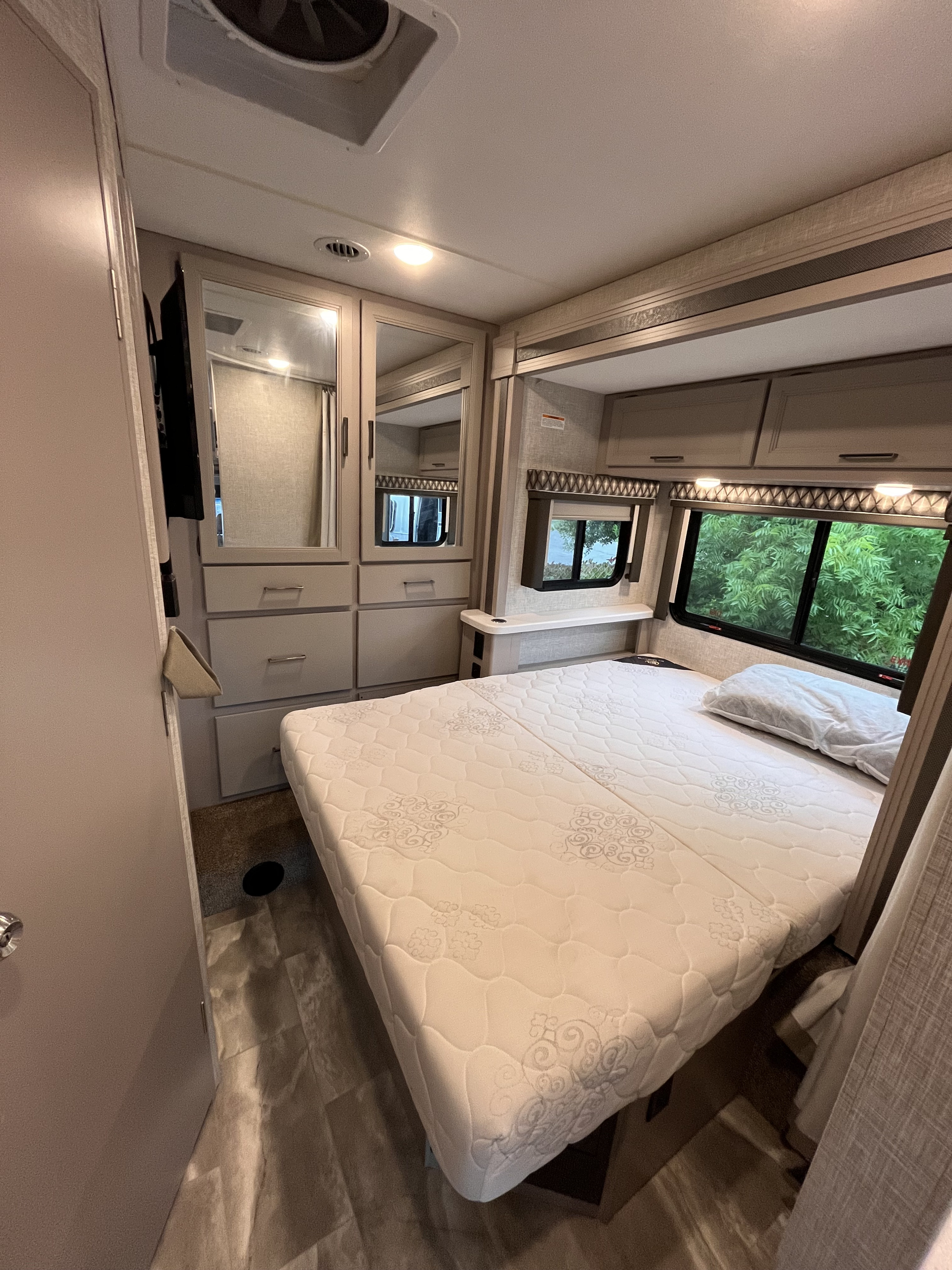 Enjoy a comfortable RV rental bedroom with a queen bed, ample storage, and scenic window views for your travels.. Thor Quantum 2022