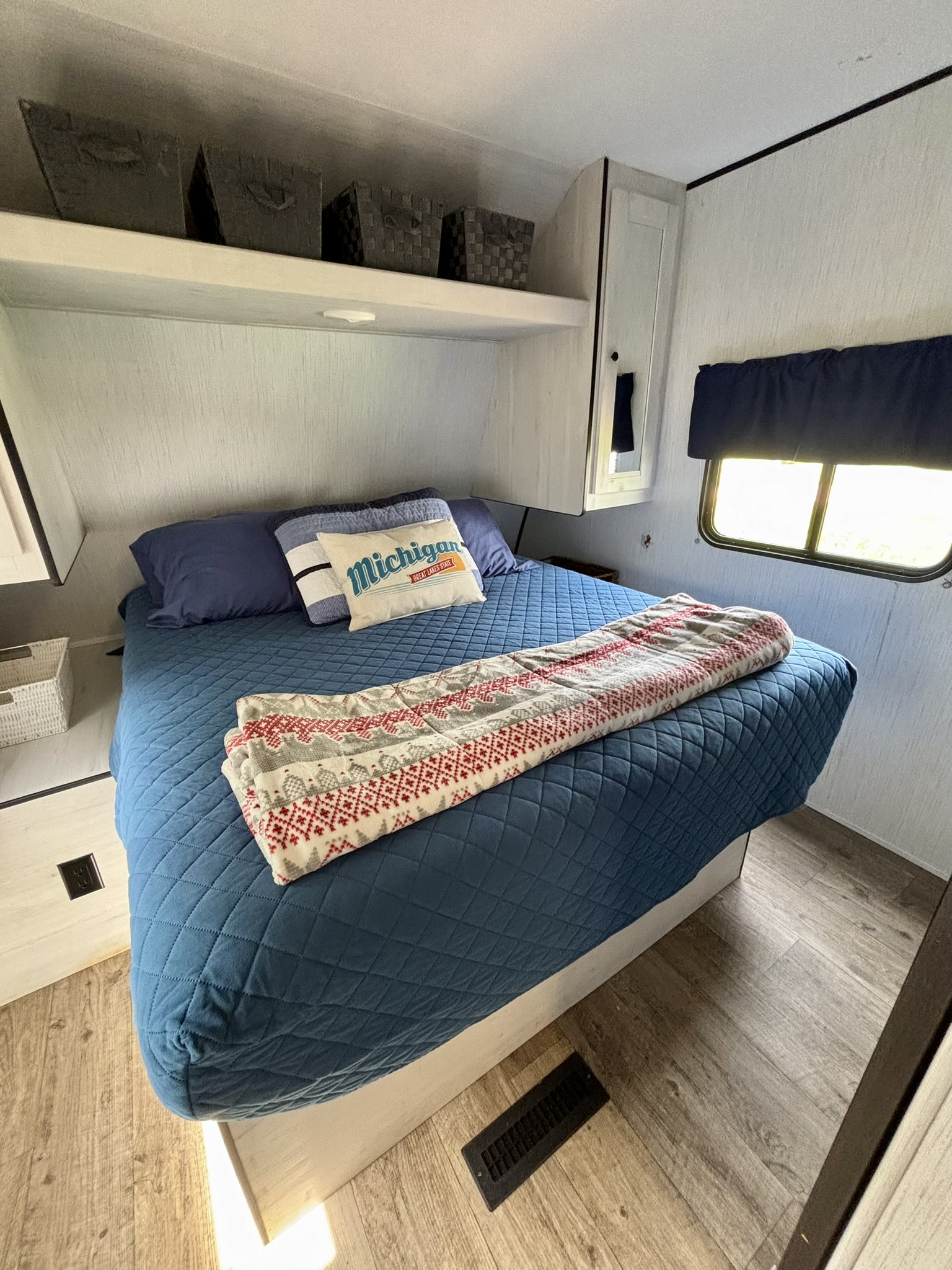 Cozy RV rental bedroom features a blue quilted bedspread, 'Michigan' pillow, and overhead storage. Ideal for travel.. Heartland RVs Trail Runner 2021