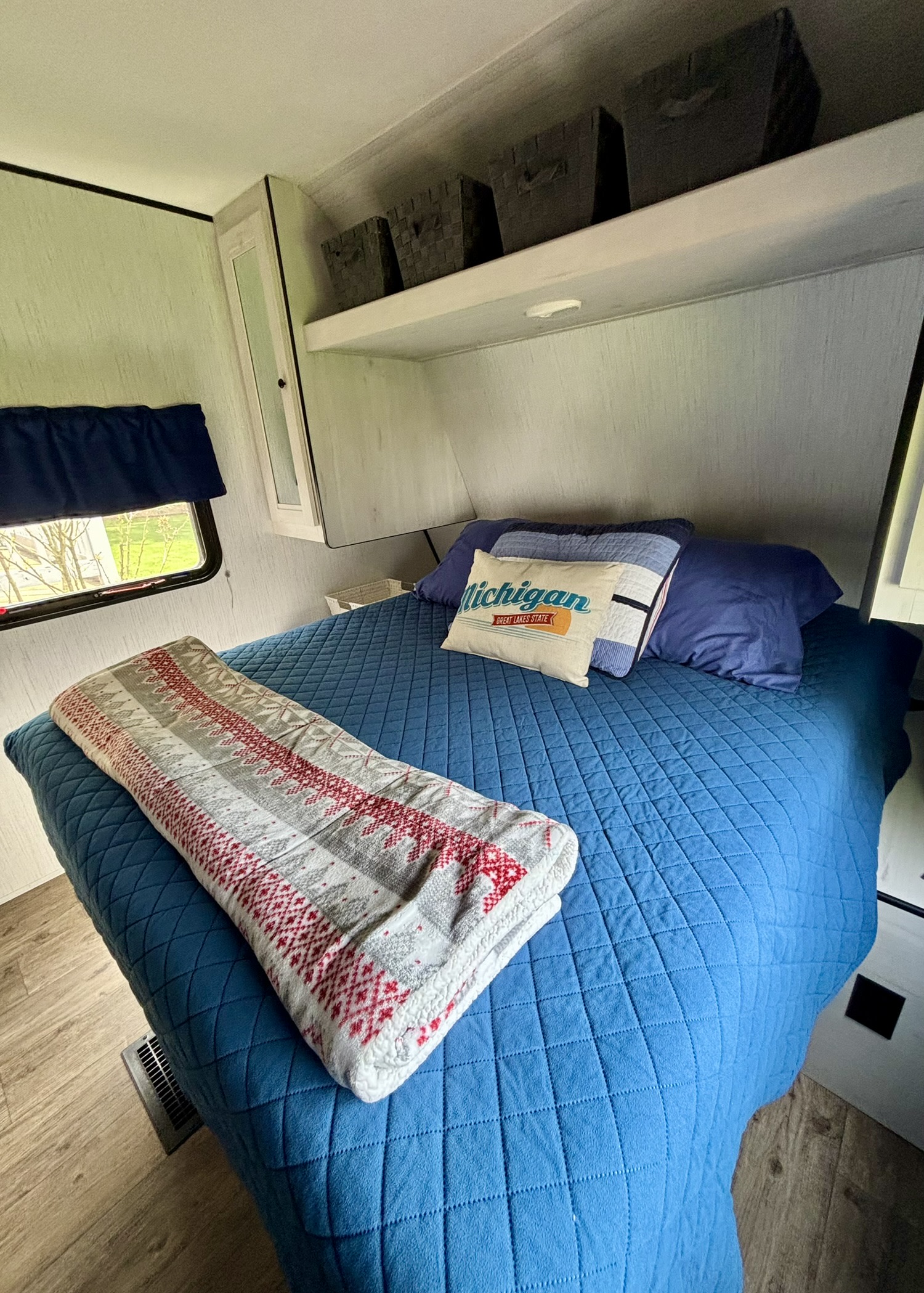 Comfortable RV rental bedroom with blue bed, Michigan pillow, storage, & window. Ideal for travel adventures.. Heartland RVs Trail Runner 2021