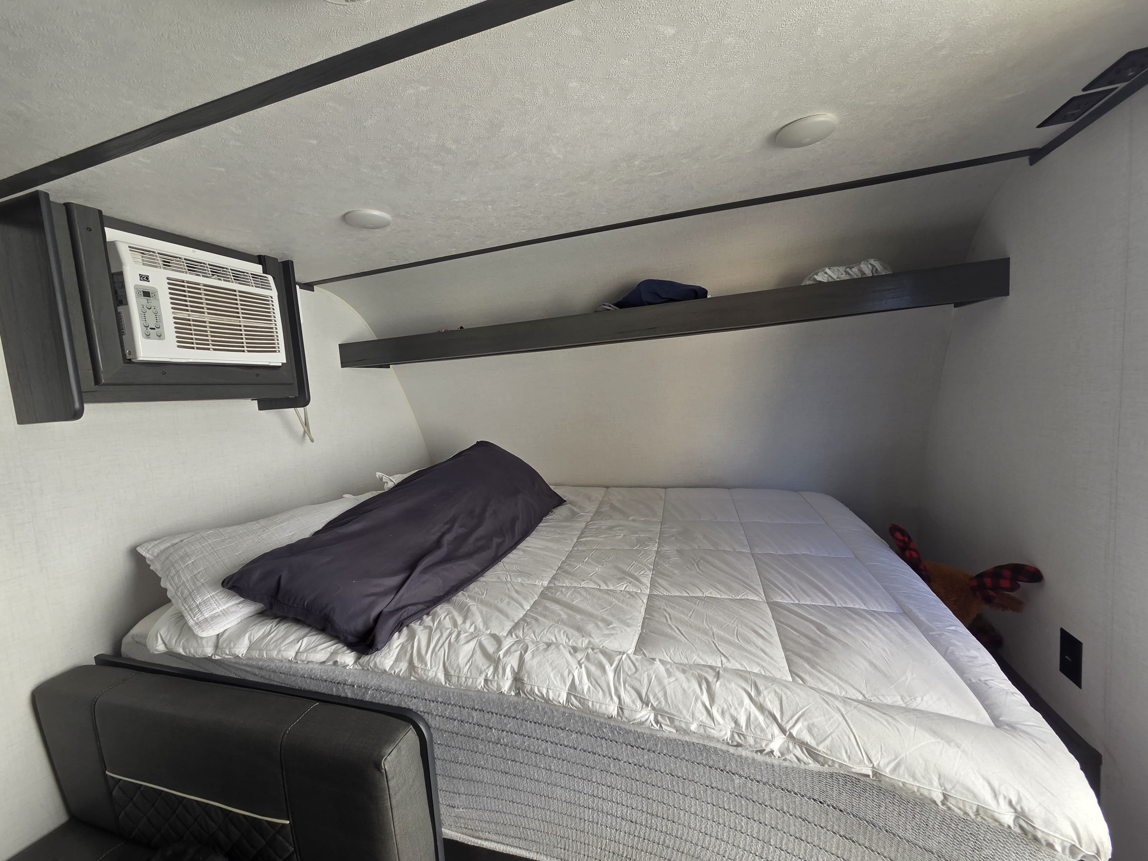 Comfortable RV rental bedroom with a white quilted bed, wall-mounted AC unit, and a small overhead storage shelf.. Aspen Trail LE 2024