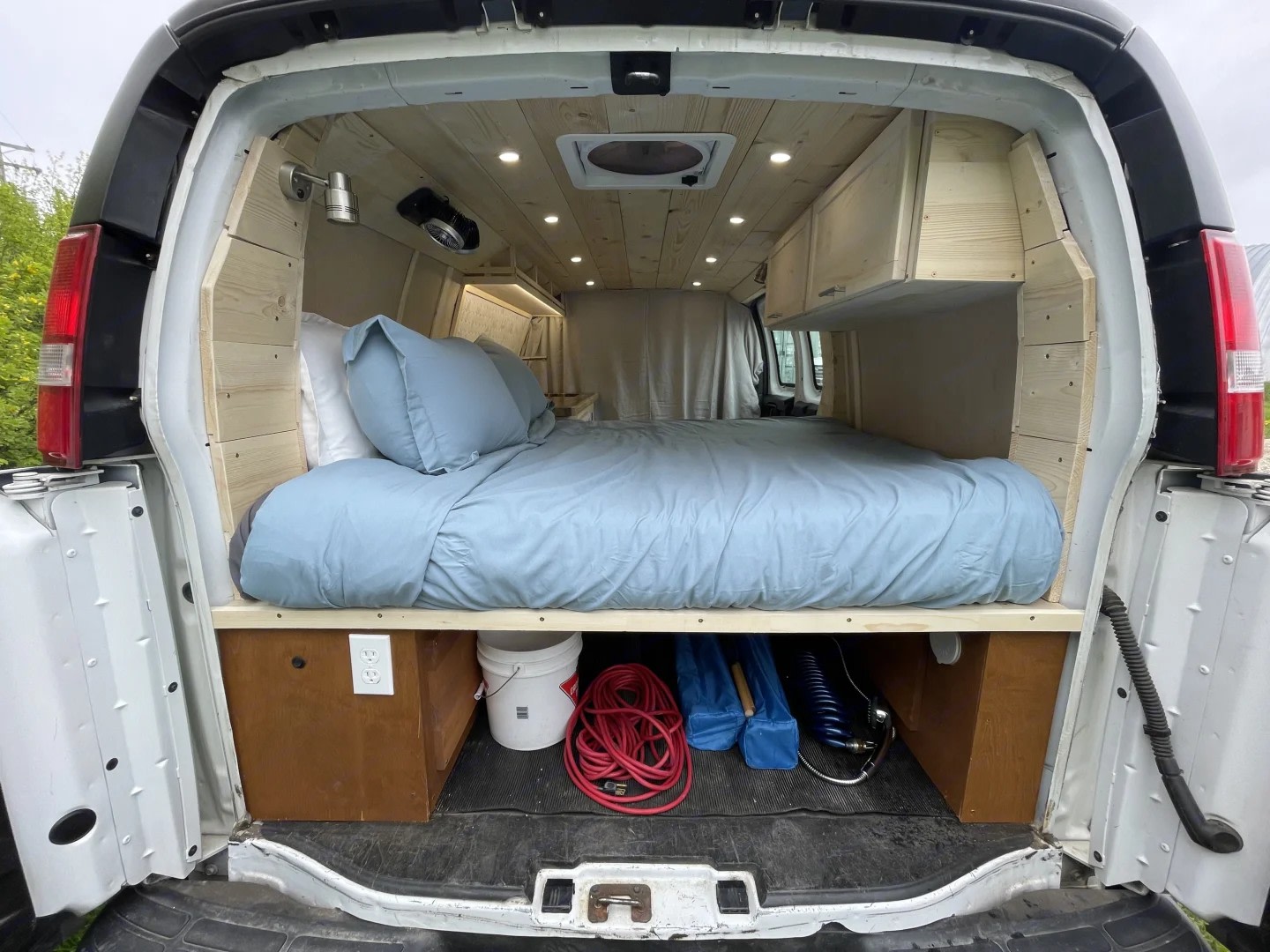 RV rental: Inside a converted van with a comfy bed, wood paneling, overhead lights, and storage below the bed.. Gmc Savanna 2500 2015