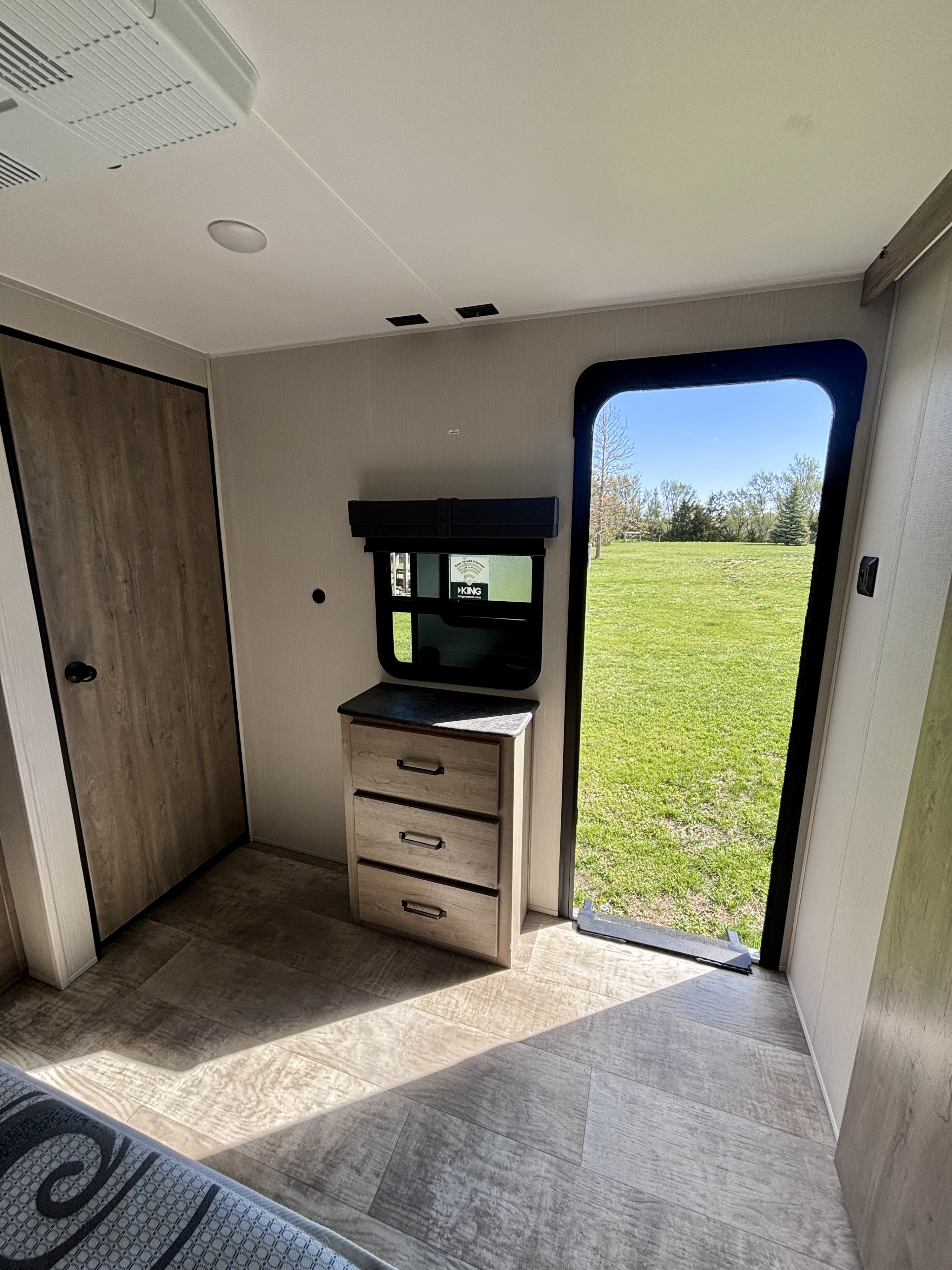 Bright RV rental interior with a door, dresser, and an open exit leading to a vibrant green outdoor scene.. Forest River Palomino Puma 2024