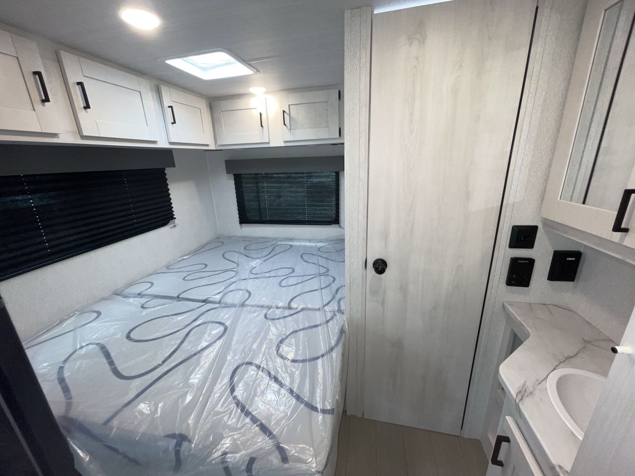 Inside a modern RV rental bedroom featuring an unused bed, overhead cabinets, and a convenient adjacent vanity area.. Forest River Entrada 2026