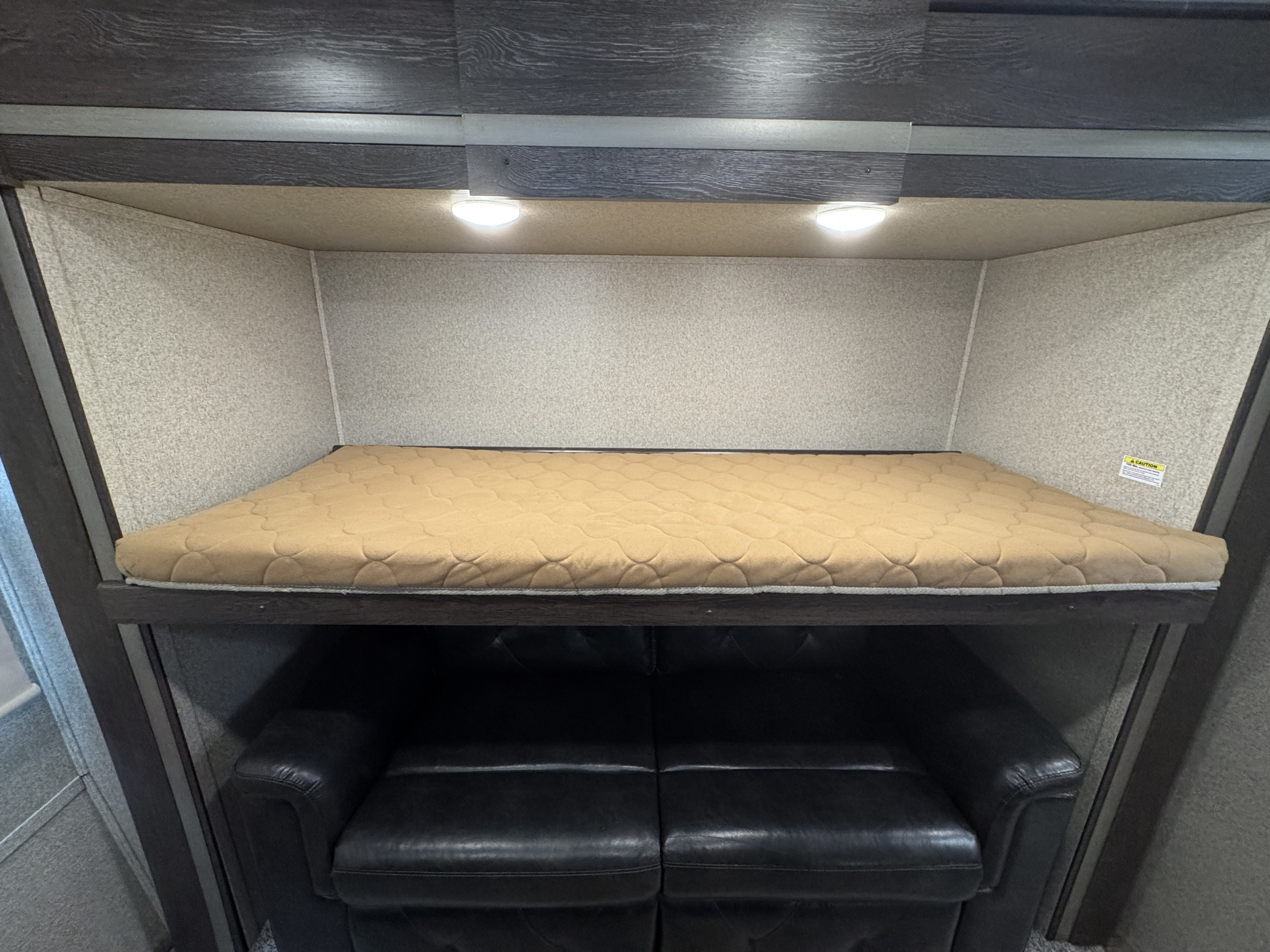 This **RV rental** features a cozy bunk bed with overhead lighting, neatly stacked above a dark, comfortable sofa.. Keystone Outback 2019