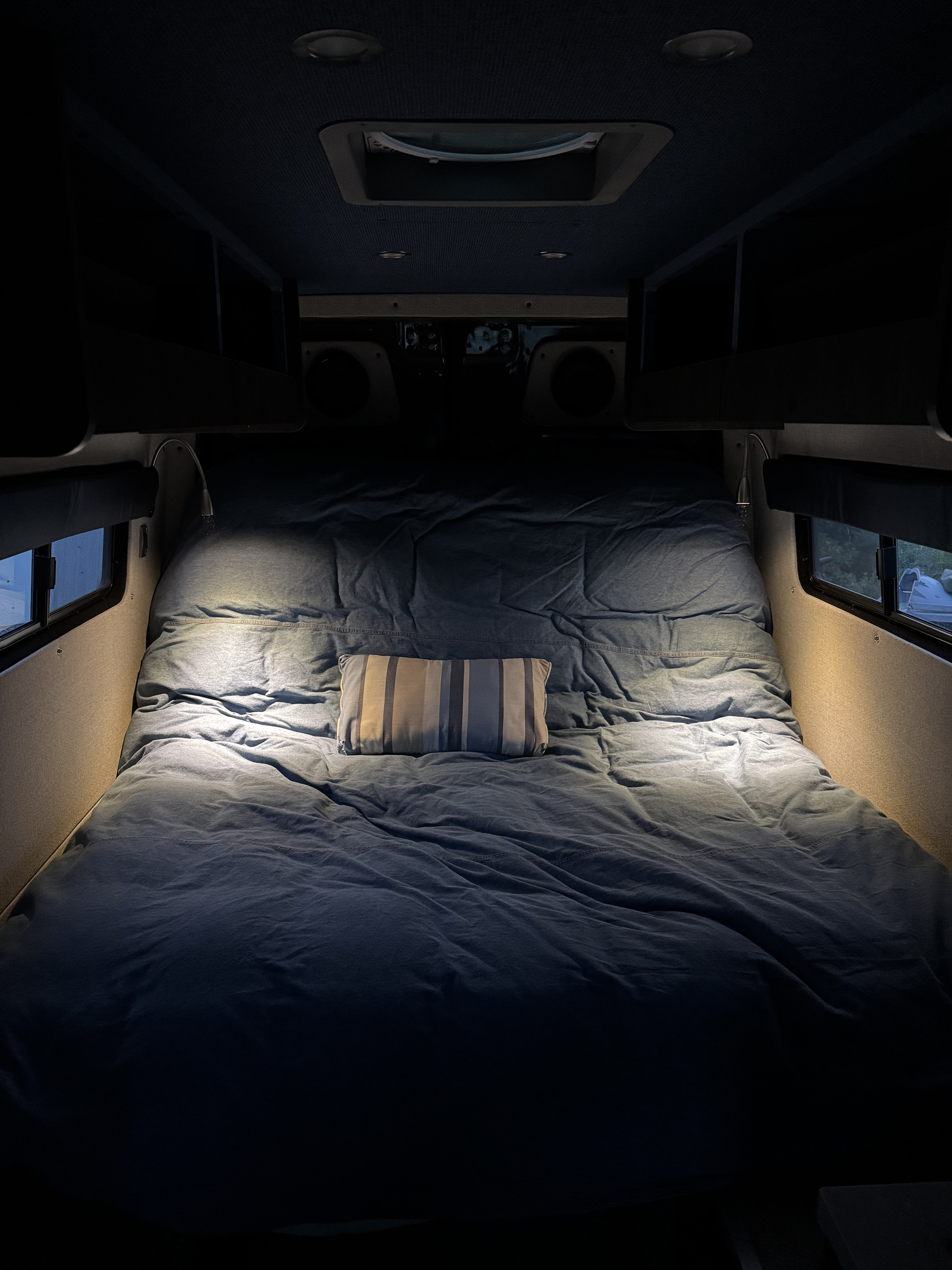 This RV rental's cozy bed features denim-blue bedding, a striped pillow, and bright reading lights for comfortable travels.. Mercedes Sprinter 2020