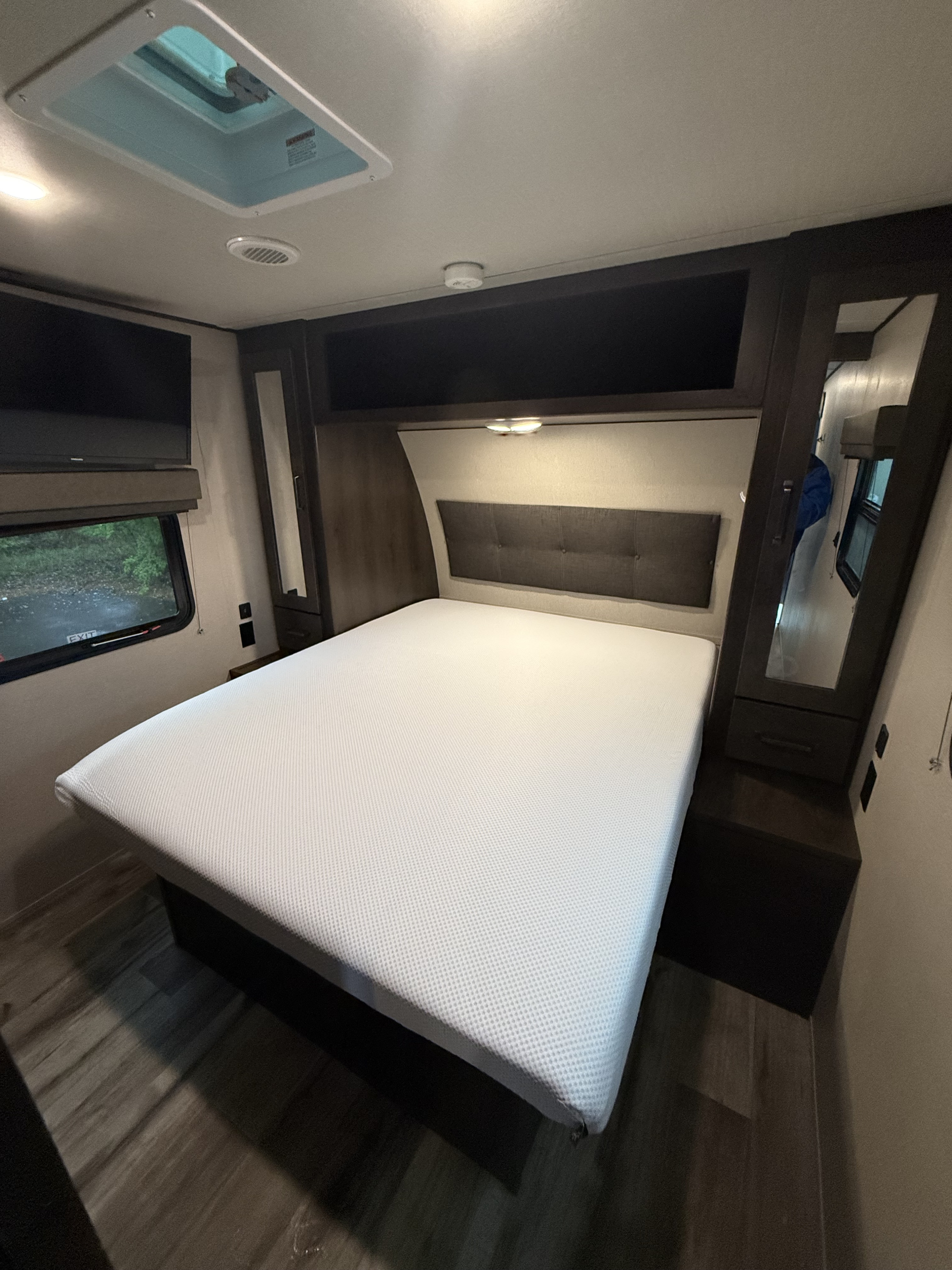 A well-appointed RV rental bedroom features a fresh white mattress, headboard, TV, window, and mirrored wardrobe for your travels.. Grand Design Transcend Xplor 2022