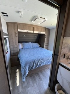 Spacious RV rental bedroom with a queen bed, overhead storage, and AC unit for your comfortable travel adventures.. Grand Design Imagine 2022