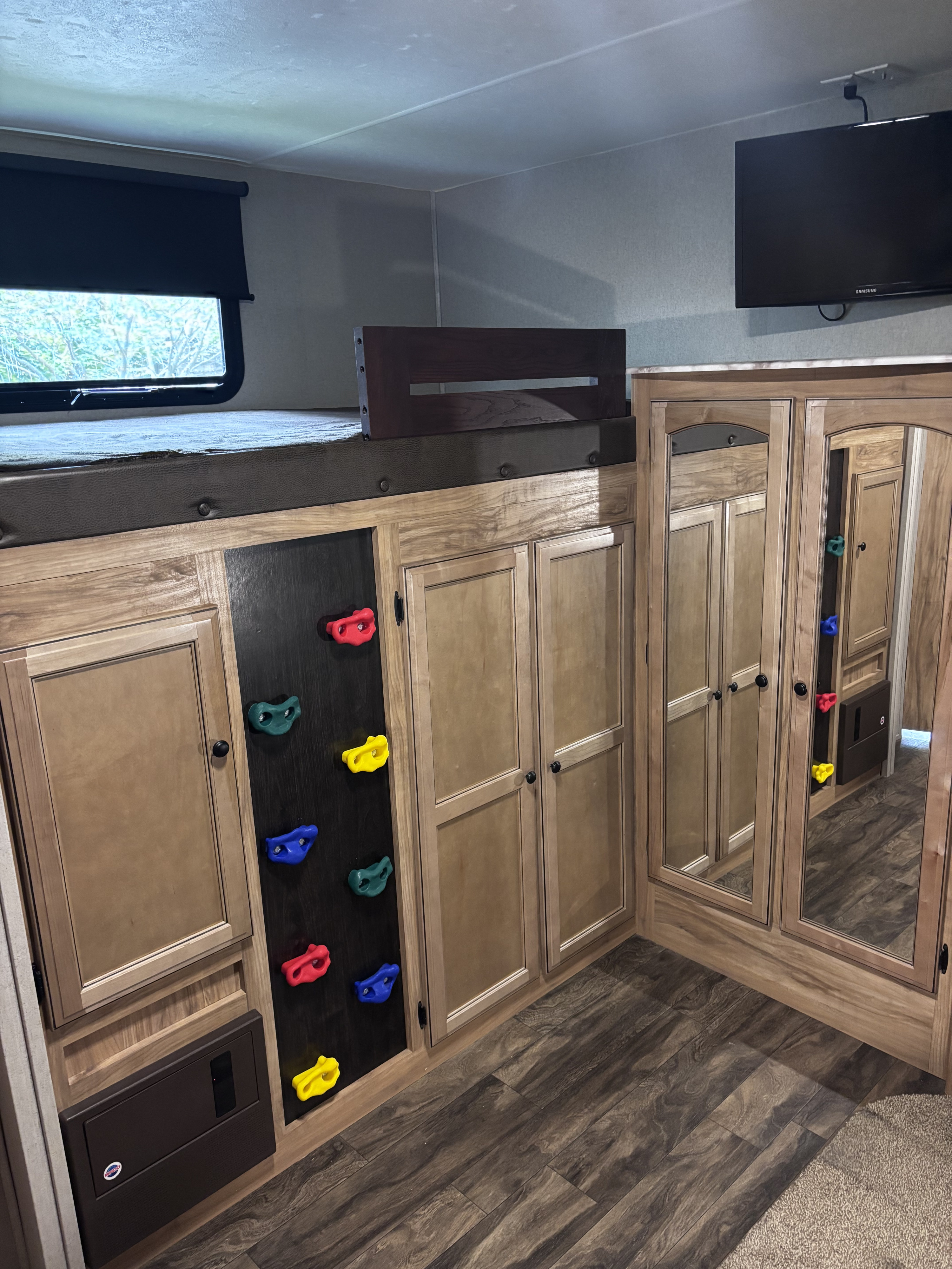 Experience an RV rental! This image shows a bunk bed with a colorful climbing wall ladder, storage cabinets, and a wall-mounted TV.. Coachmen Freedom Liberty Express 2018
