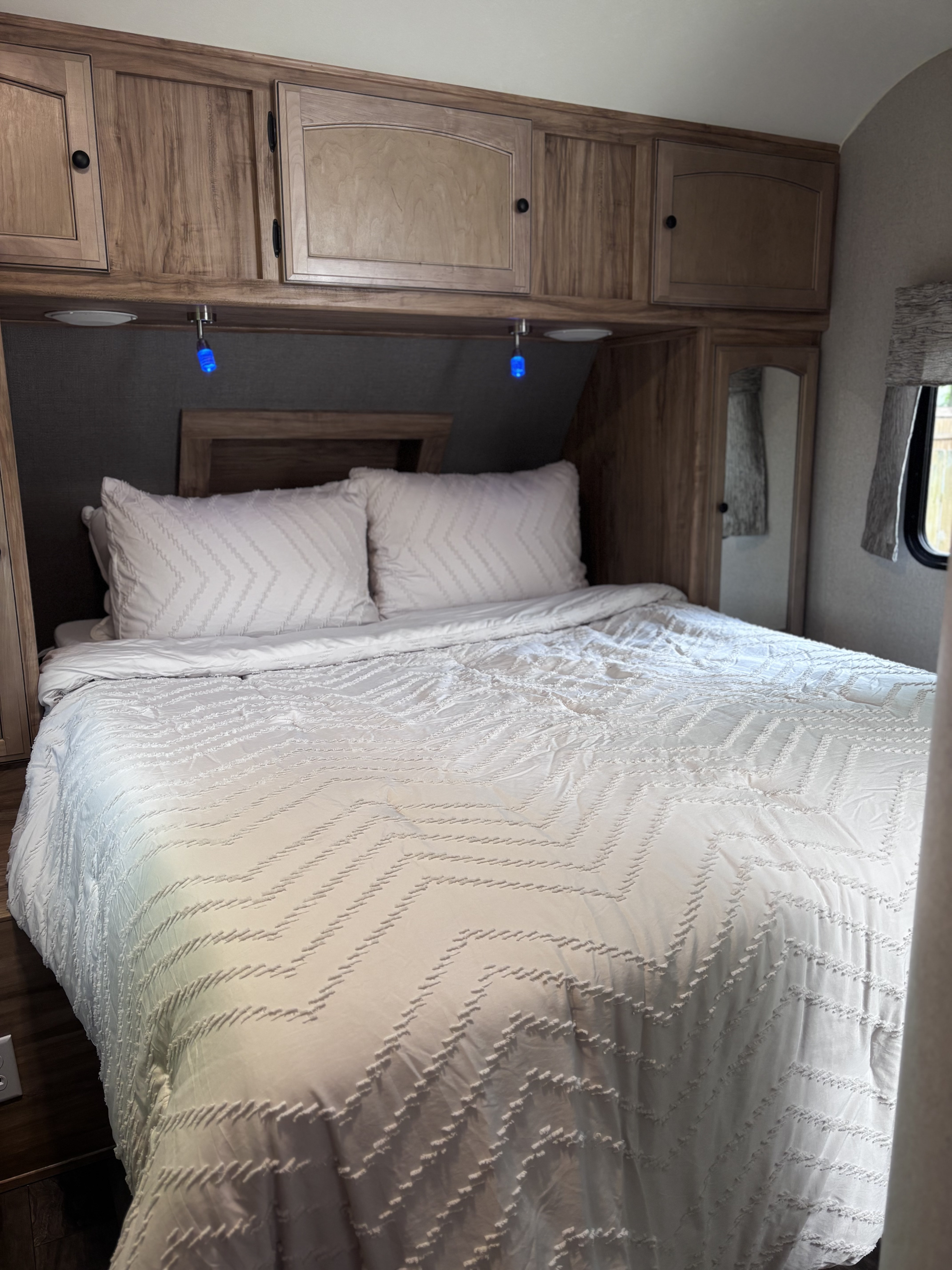 Cozy RV rental bedroom with white chevron bedding, overhead storage, and blue reading lights for a comfortable stay.. Coachmen Freedom Liberty Express 2018