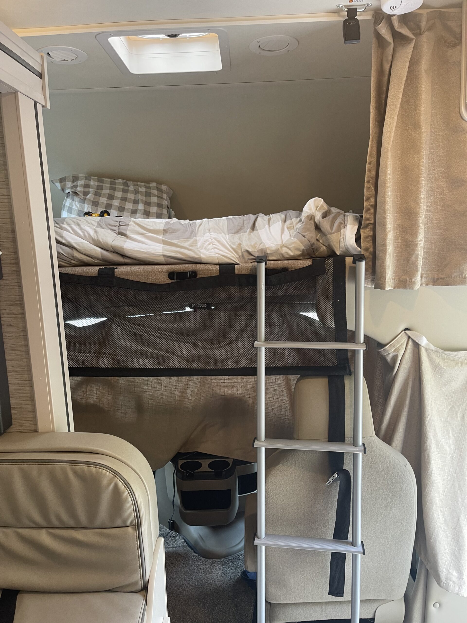 Cozy RV rental interior showing a top bunk bed with ladder, comfortable front seats, and overhead features.. Thor Chateau 2021