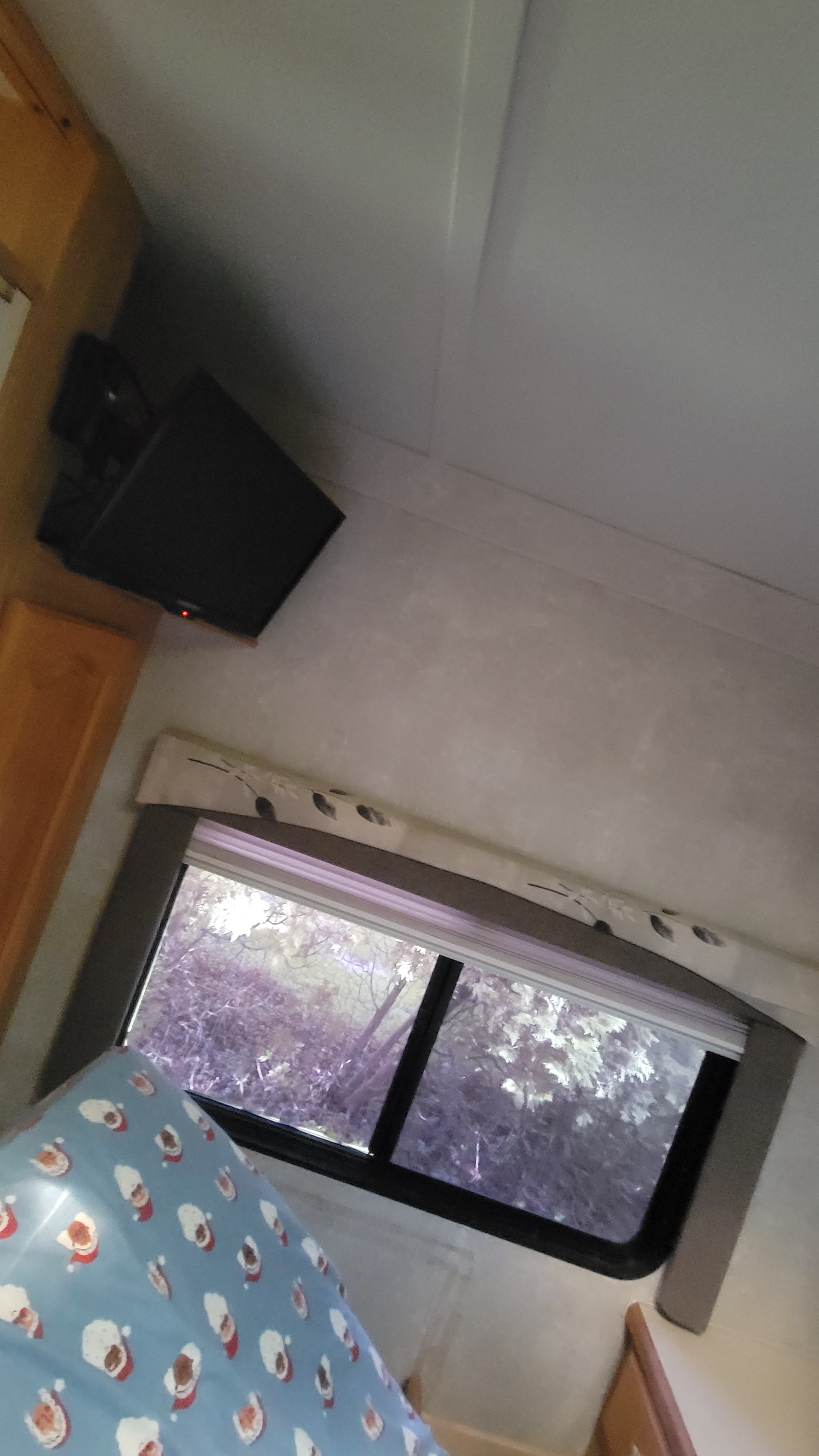 Cozy RV rental interior: bedroom with festive Santa sheet, window view, and wall-mounted TV.. Forest River Sunseeker 2003