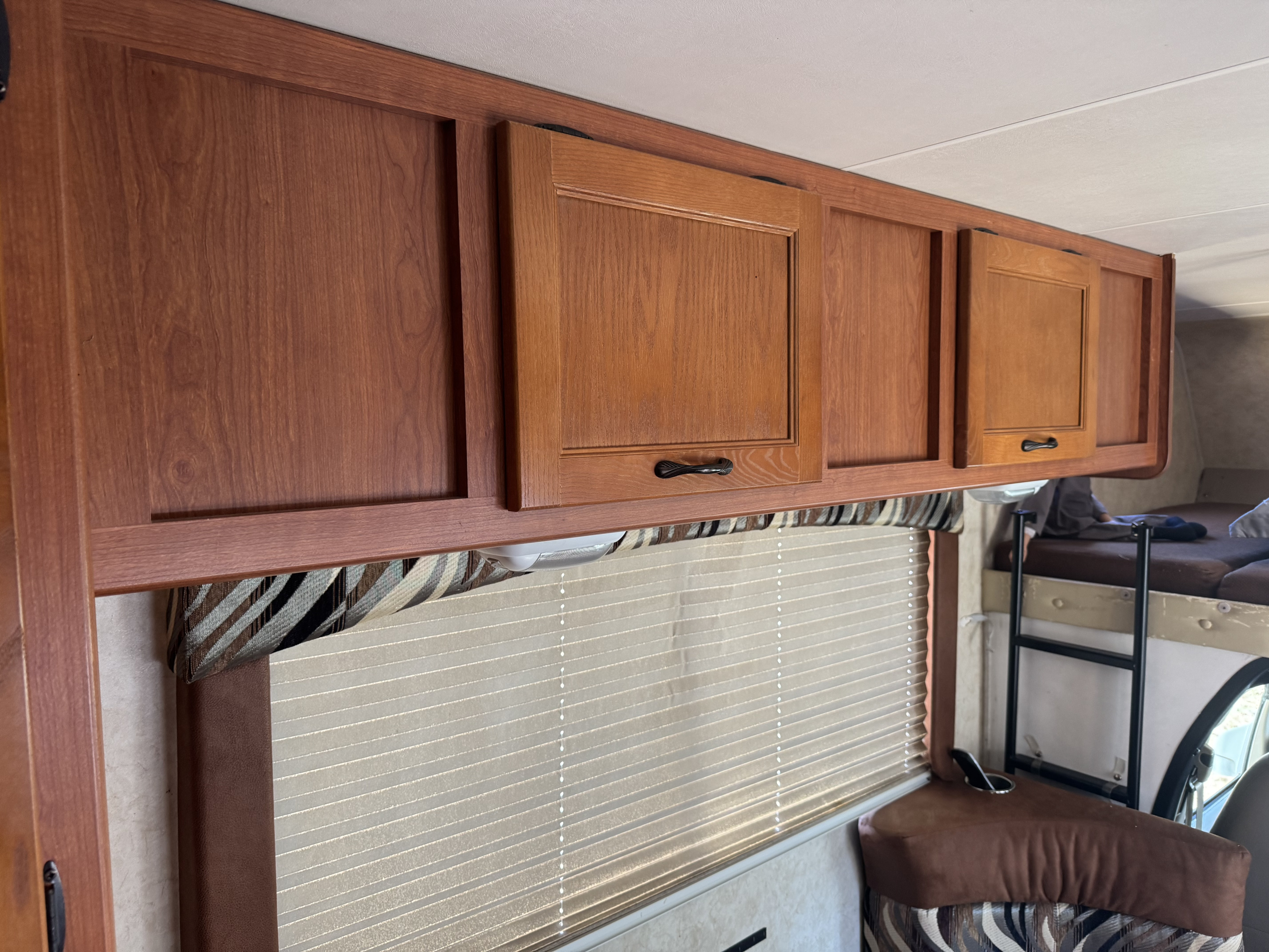 This RV rental interior features overhead wooden cabinets, a striped valance, pleated window blinds, and a bunk bed.. Coachman Freelander 21QB Chevy 4500 2013