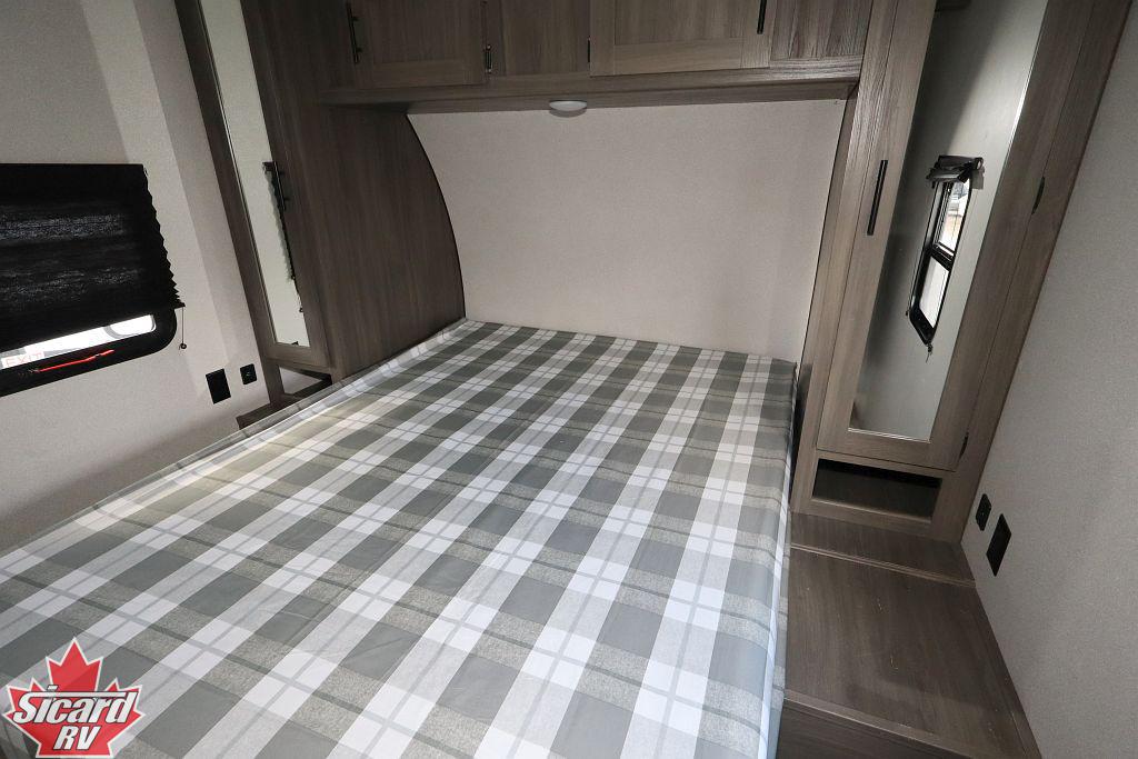 Comfortable RV rental bedroom featuring a plaid bed, overhead cabinets, and mirrored side storage for your travels.. Forest River Grand River 2022