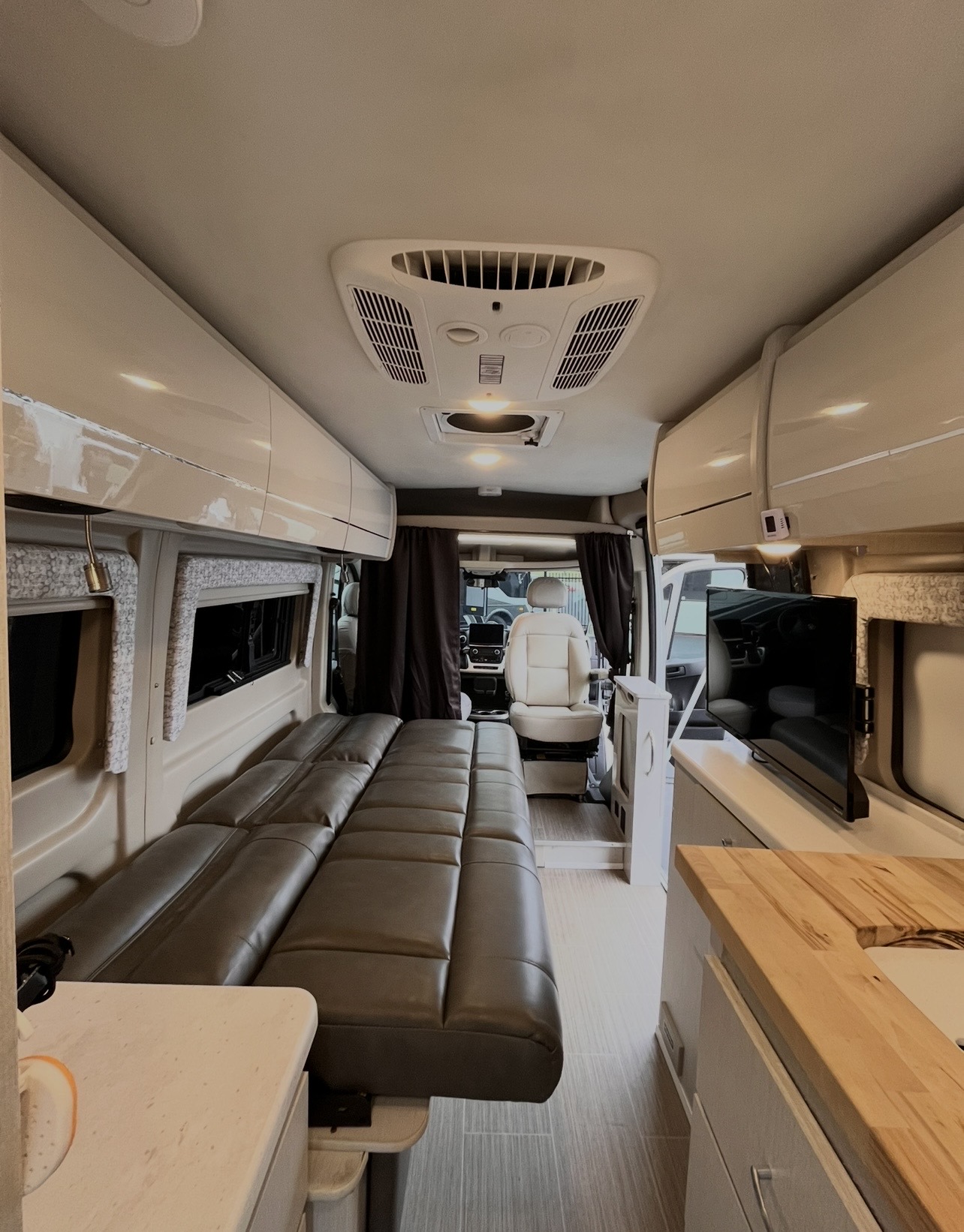 Inside a comfortable rv rental: showing a lounge bed, kitchen counter with sink, wall-mounted TV, and front cabin view.. Thor Tellaro 2023