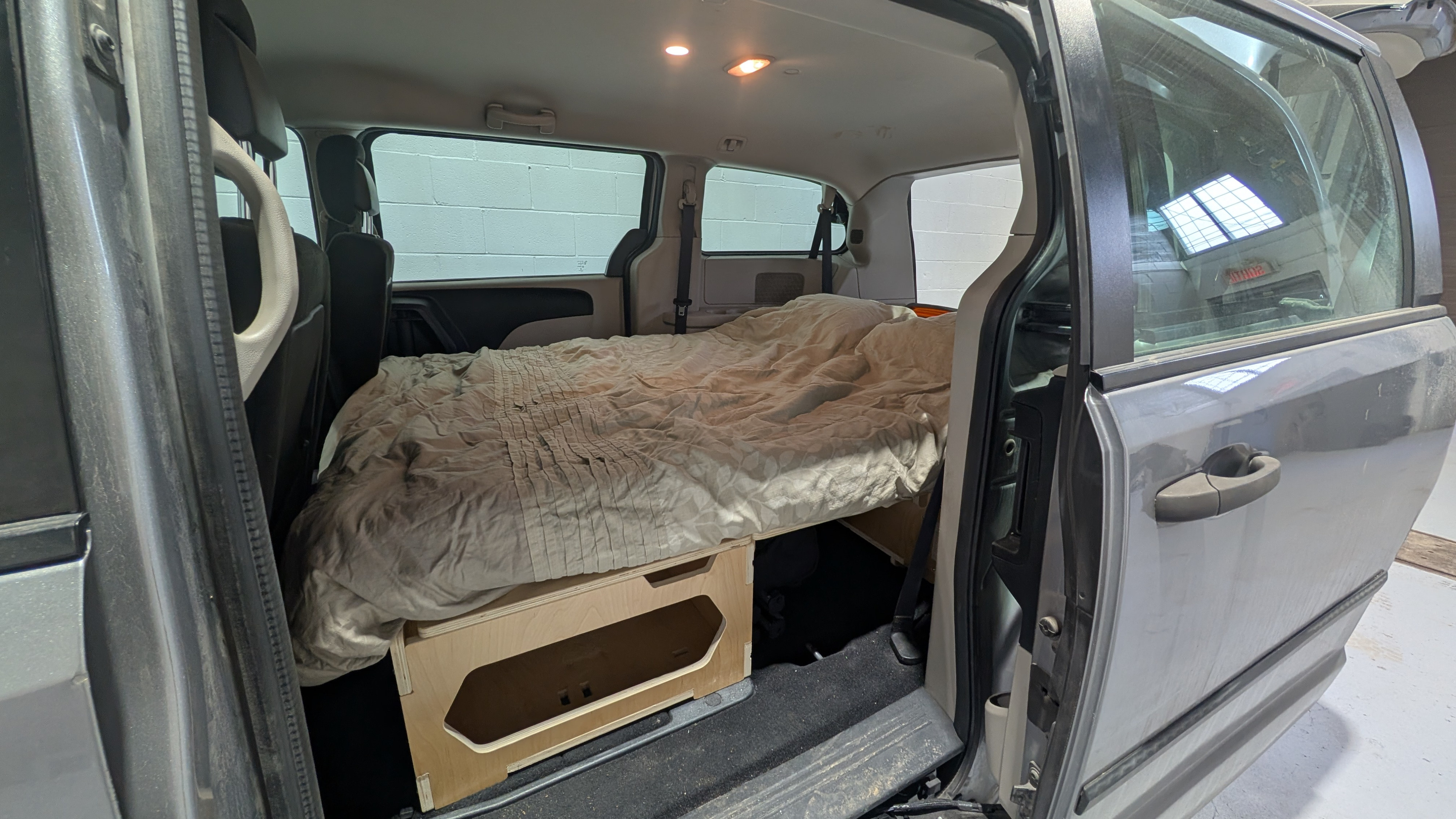 Minivan camper conversion: a bed over wooden storage units, ideal for an rv rental or van travel.. Dodge Grand Caravan 2016