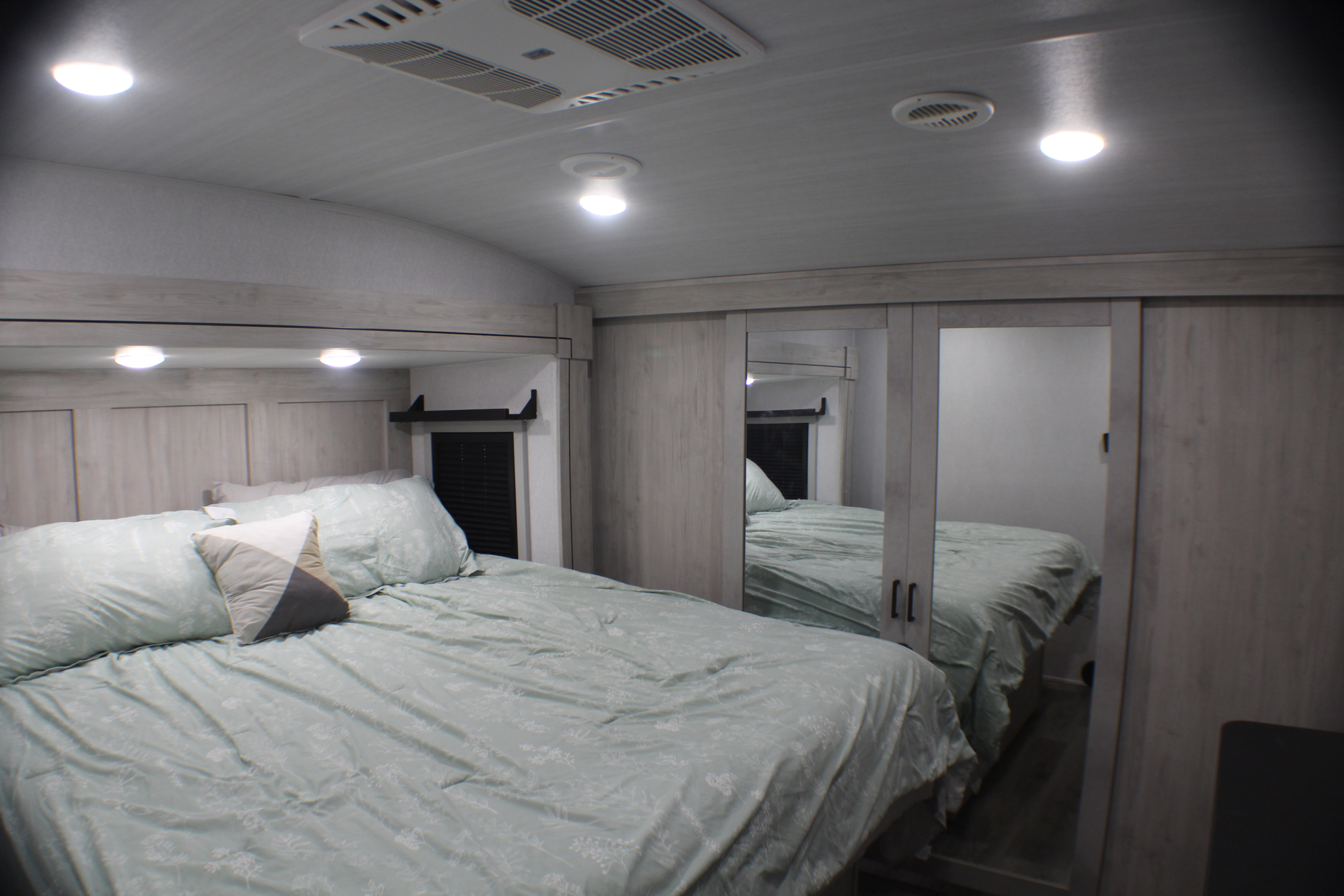 Comfortable RV rental bedroom featuring light green bedding, overhead lights, and mirrored closet for storage.. East to West Blackthorn 2025