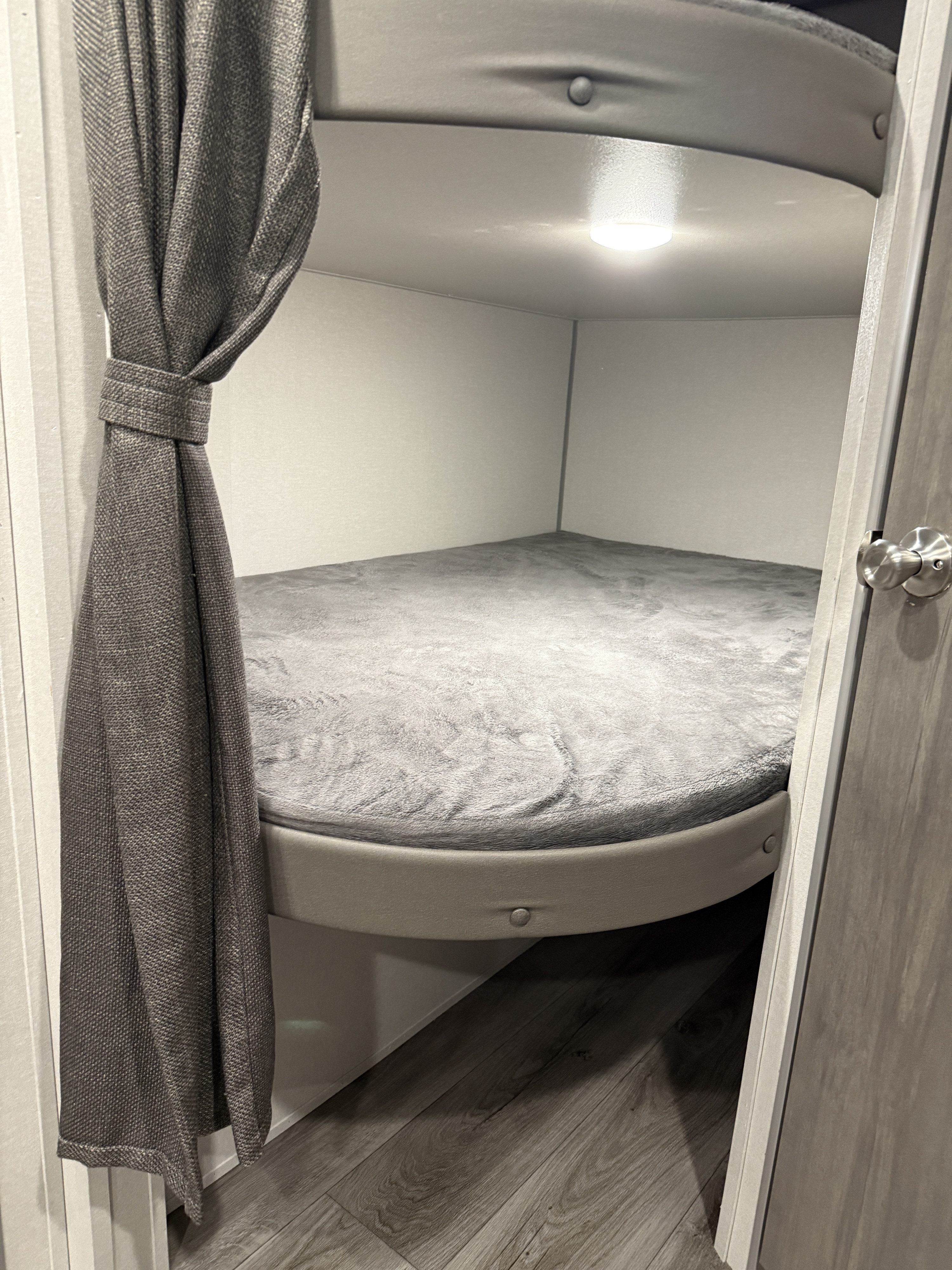 Cozy RV rental bunk bed with a soft grey mattress, a tied-back curtain, and an overhead light for comfortable sleeping.. Forest River Coachmen Catalina Summit 2025