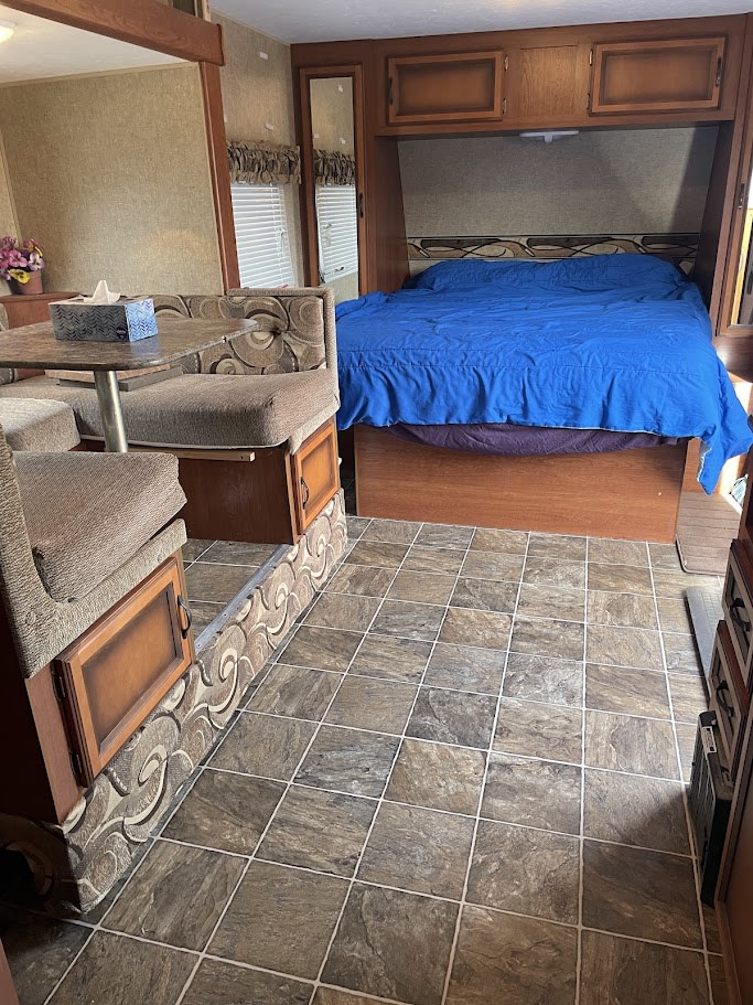 Explore this RV rental's inviting interior: a comfortable bed with blue bedding and a dinette area for meals.. Sportsmen Show Stopper 2015