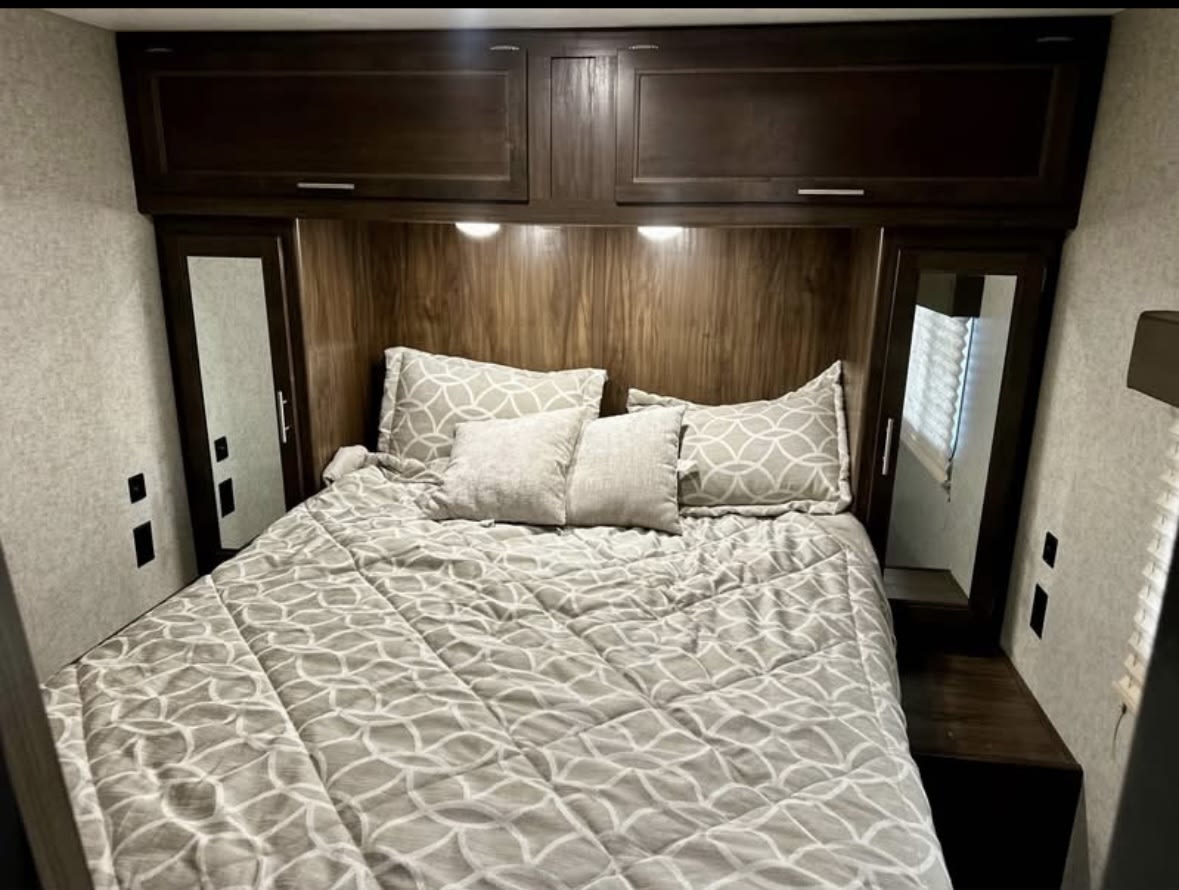 Cozy RV rental bedroom features a comfy bed, dark wood cabinets, and built-in storage. Ideal for road trips and travel.. Forest River Cherokee 2017