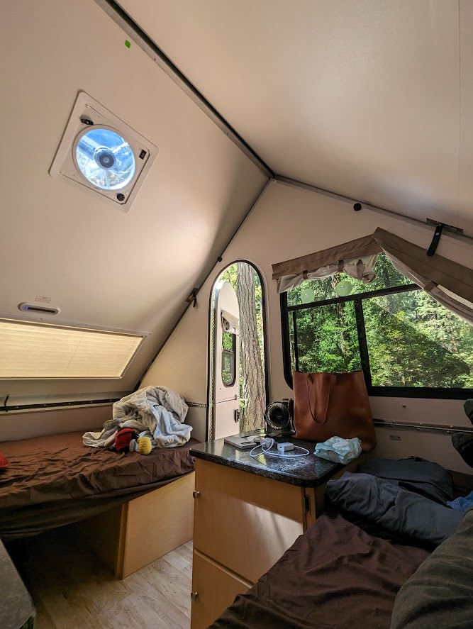 Inside a cozy rv rental bedroom with dual beds, storage, and a scenic nature view from the windows.. A Liner A Liner Popup Trailer 2022