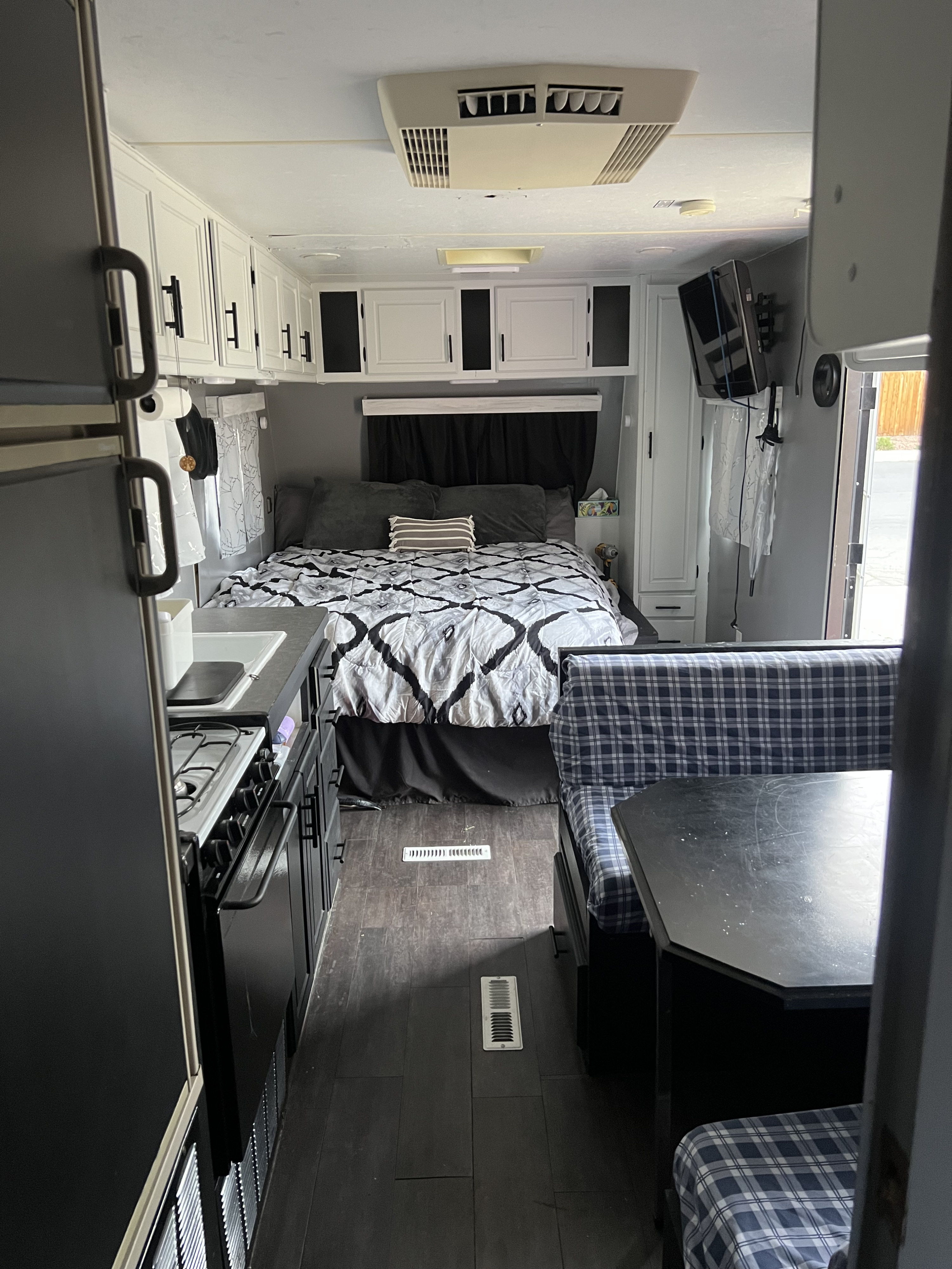 Interior of an RV rental featuring a cozy bedroom, compact kitchen with stove, and plaid dining booth. Modern and functional space.. Nash Nash Trailer 2008