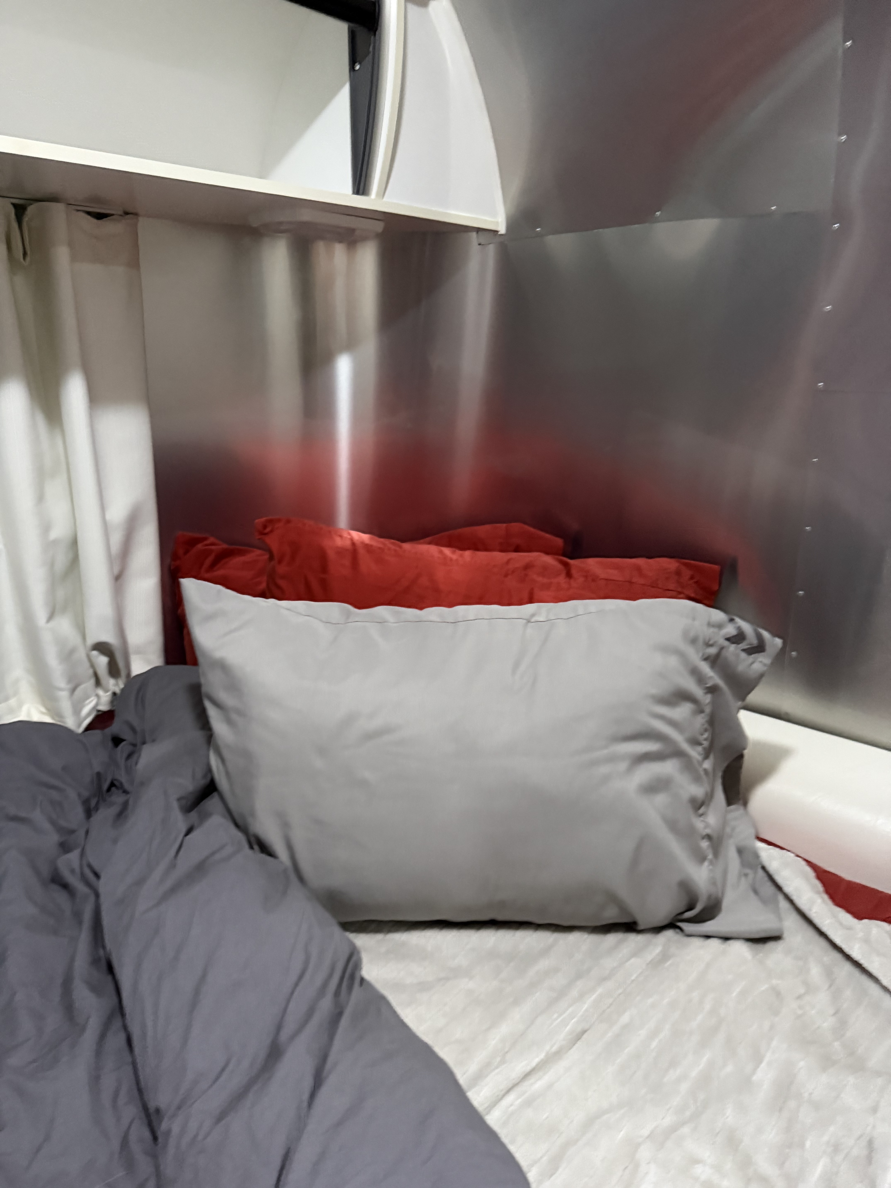 Comfortable RV rental bed with grey duvet, red & grey pillows, set against the metallic interior of an Airstream trailer.. Airstream Sport 2016