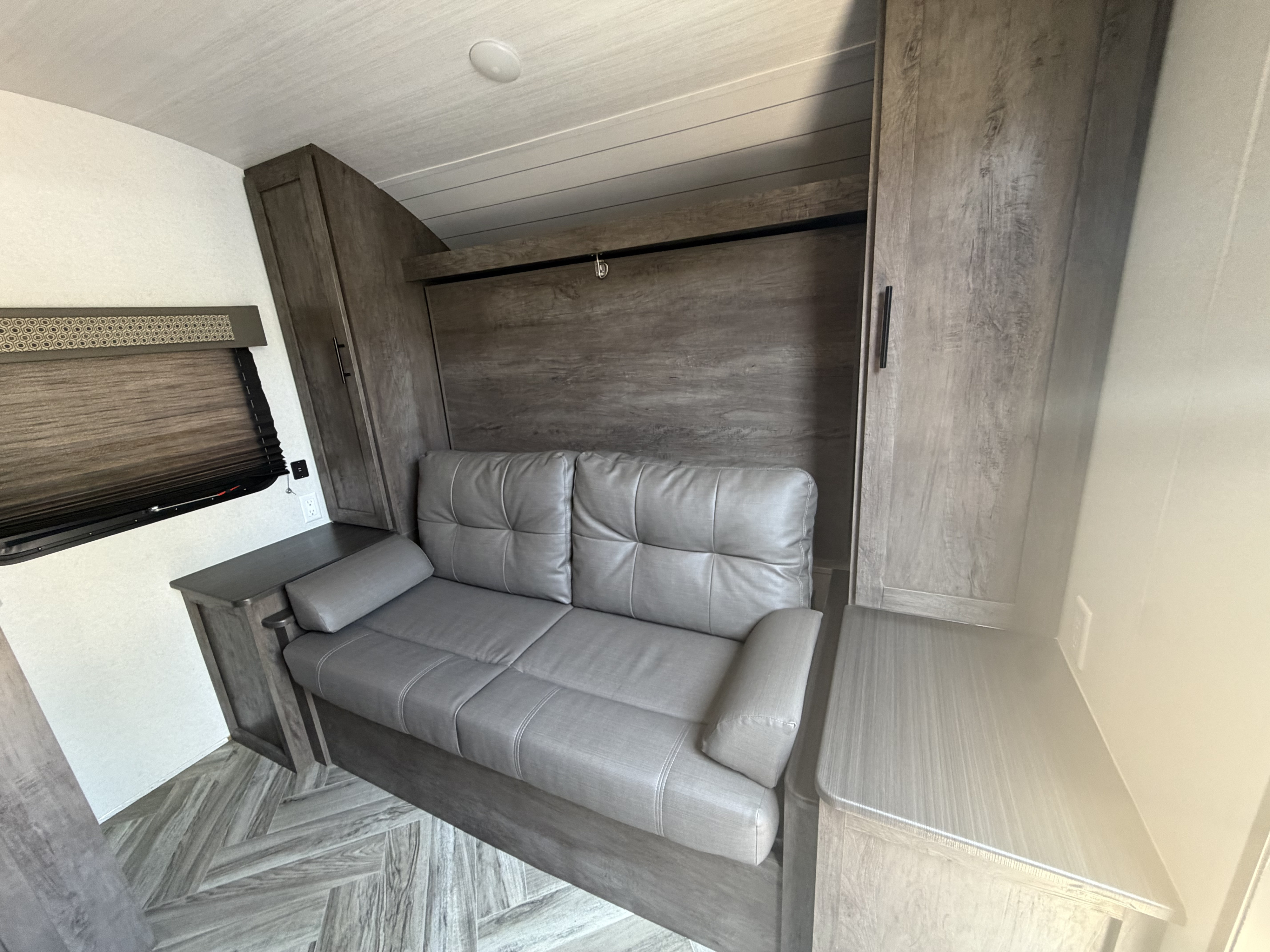 Inviting rv rental interior with a gray sofa, storage cabinets, and a clever murphy bed system for guests.. Forest River Salem Select 2021
