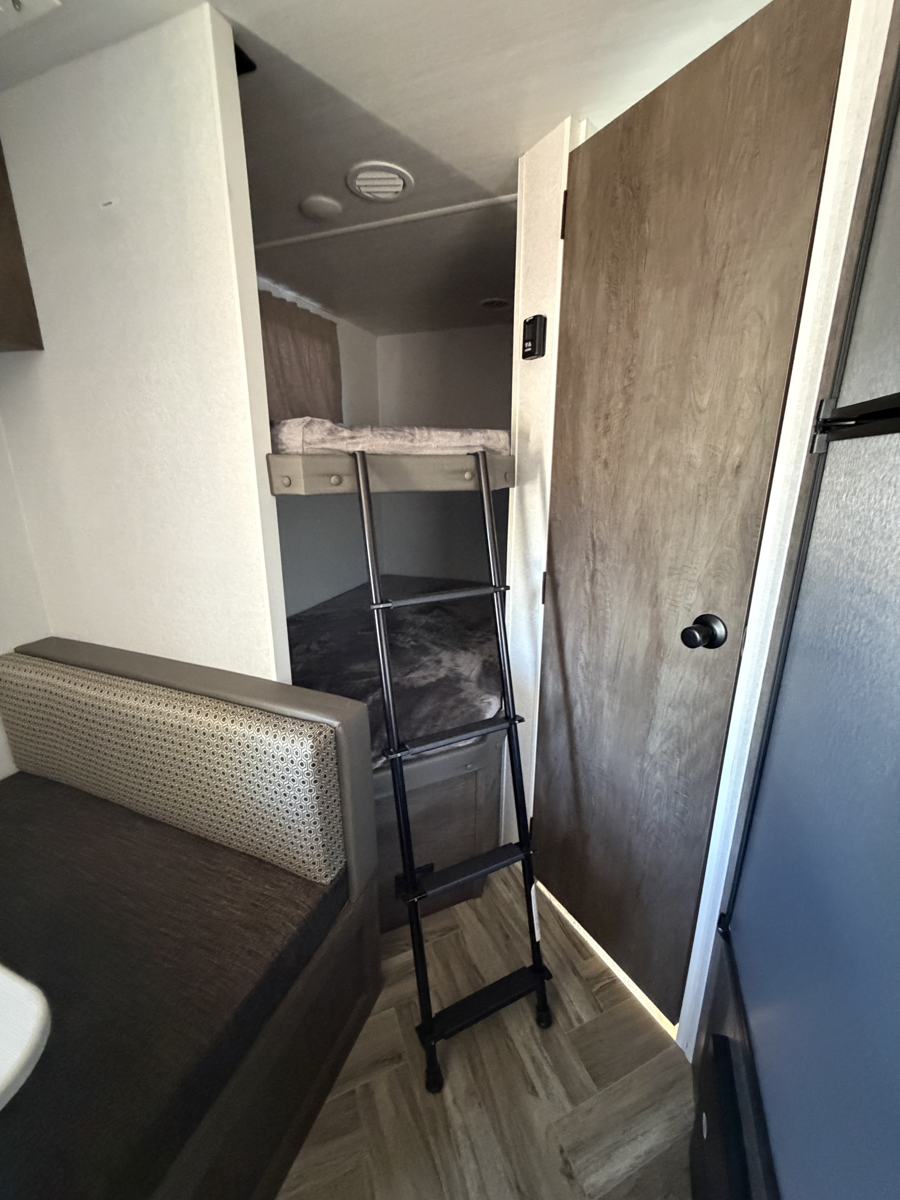 RV rental interior: bunk beds with ladder, adjacent dining booth, and door on right. Compact, functional living space.. Forest River Salem Select 2021